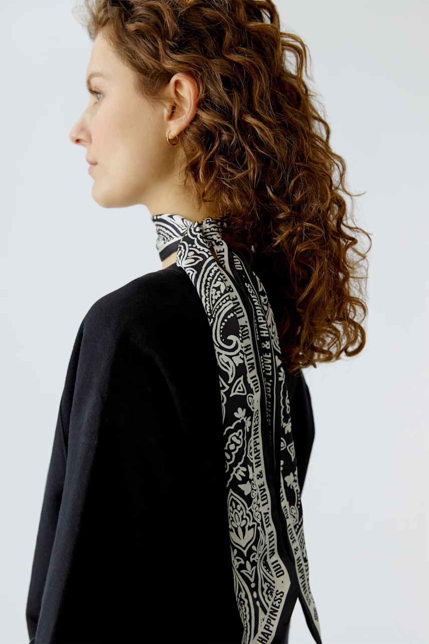 Stylish scarf: Woman wearing a patterned scarf tied at the neck, adding a unique touch to her outfit.