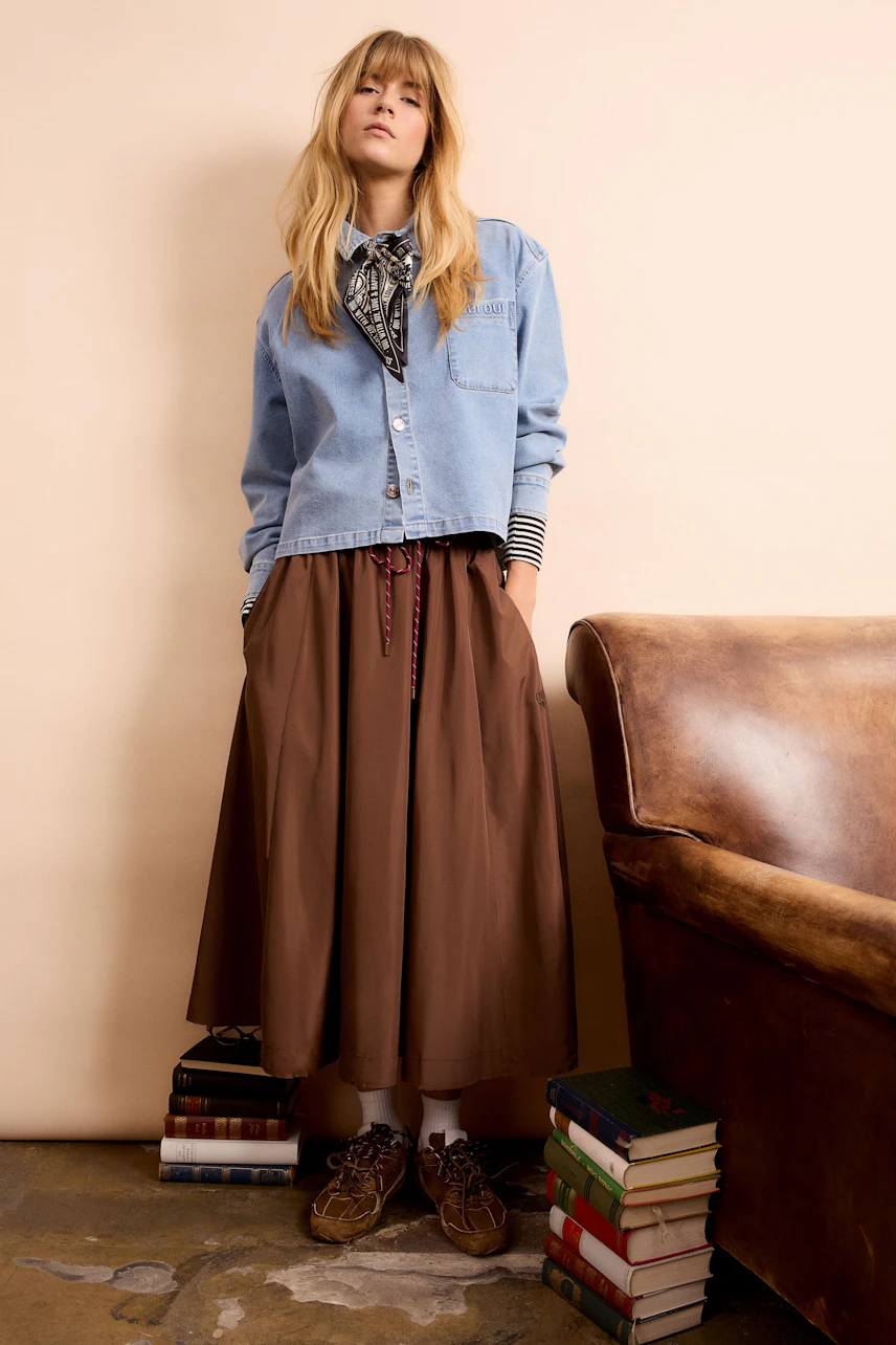 Stylish scarf: Woman wearing a patterned scarf with a denim jacket and brown skirt, standing confidently.
