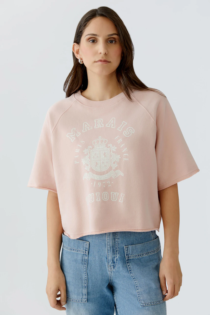 Bequemer Damen-Sweatshirt: Frau in rosa, lässigem Pullover mit grafischem Print und kurzen Ärmeln.
