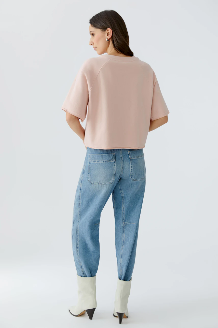 Bequemer Damen-Sweatshirt: Frau in rosa, lässigem Pullover mit kurzen Ärmeln und lockeren Jeans.