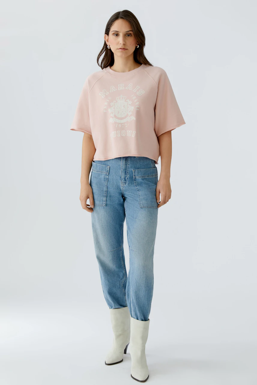 Bequemer Damen-Sweatshirt: Frau in rosa, lässigem Pullover mit grafischem Print und lockeren Jeans.