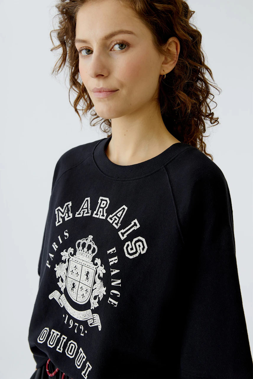Casual women's pullover: Young woman in a black sweatshirt with a graphic print, looking confidently.