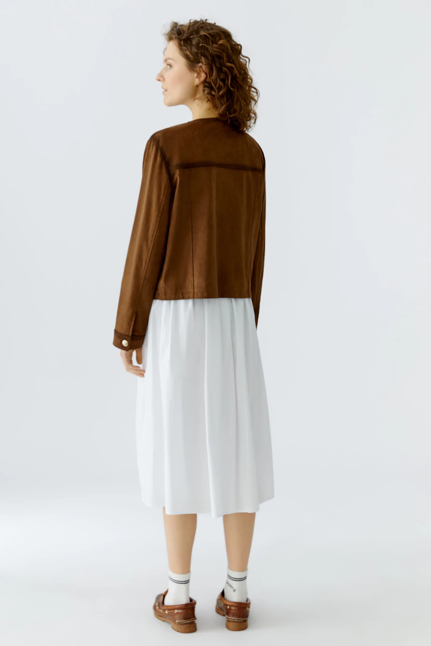 Damen Lederimitatjacke: Frau mit lockigen Haaren trägt eine braune Jacke über einem weißen Kleid.