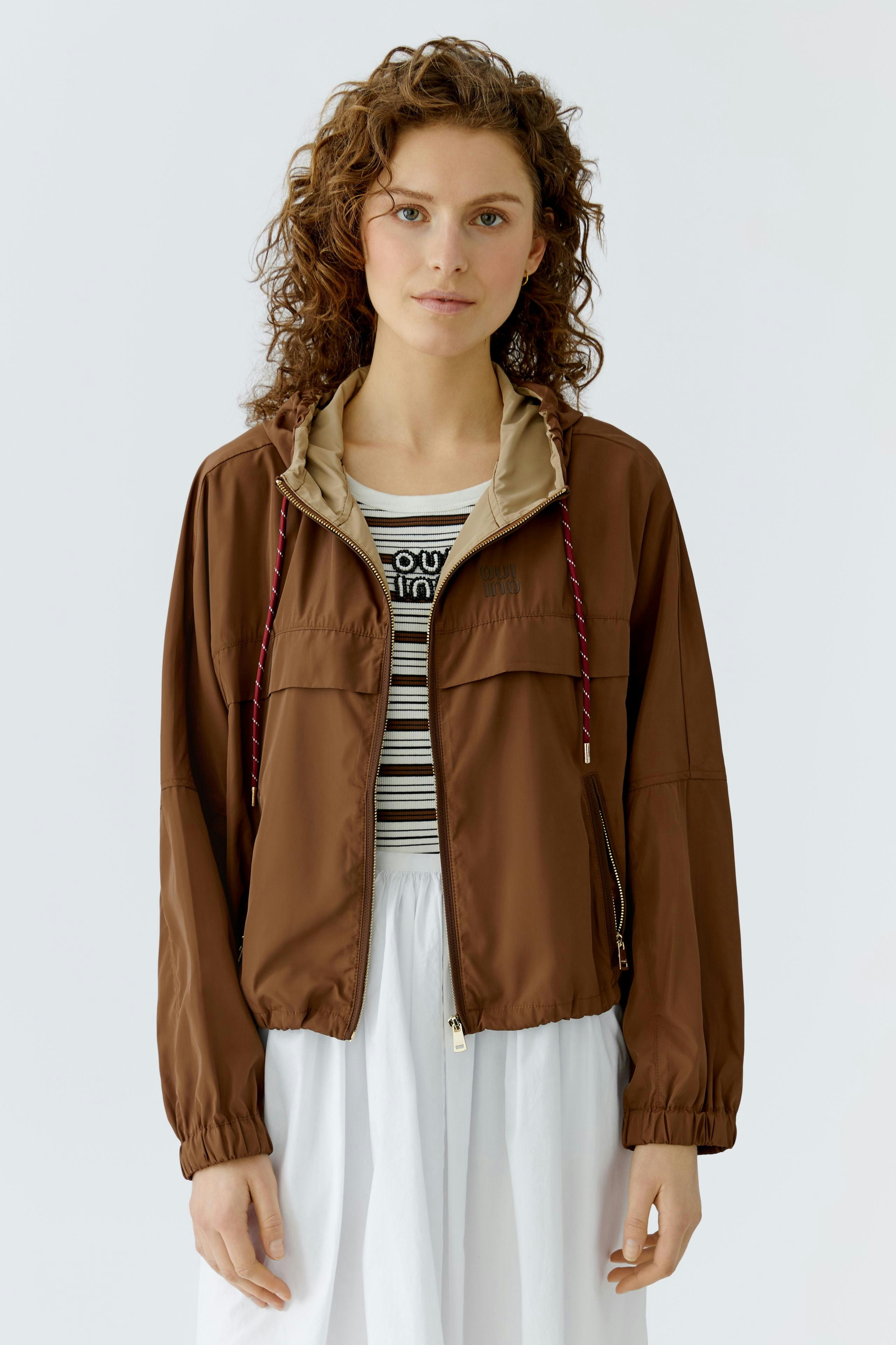 Bequeme Outdoorjacke: Frau in brauner Jacke mit Kapuze und lässigem Look.