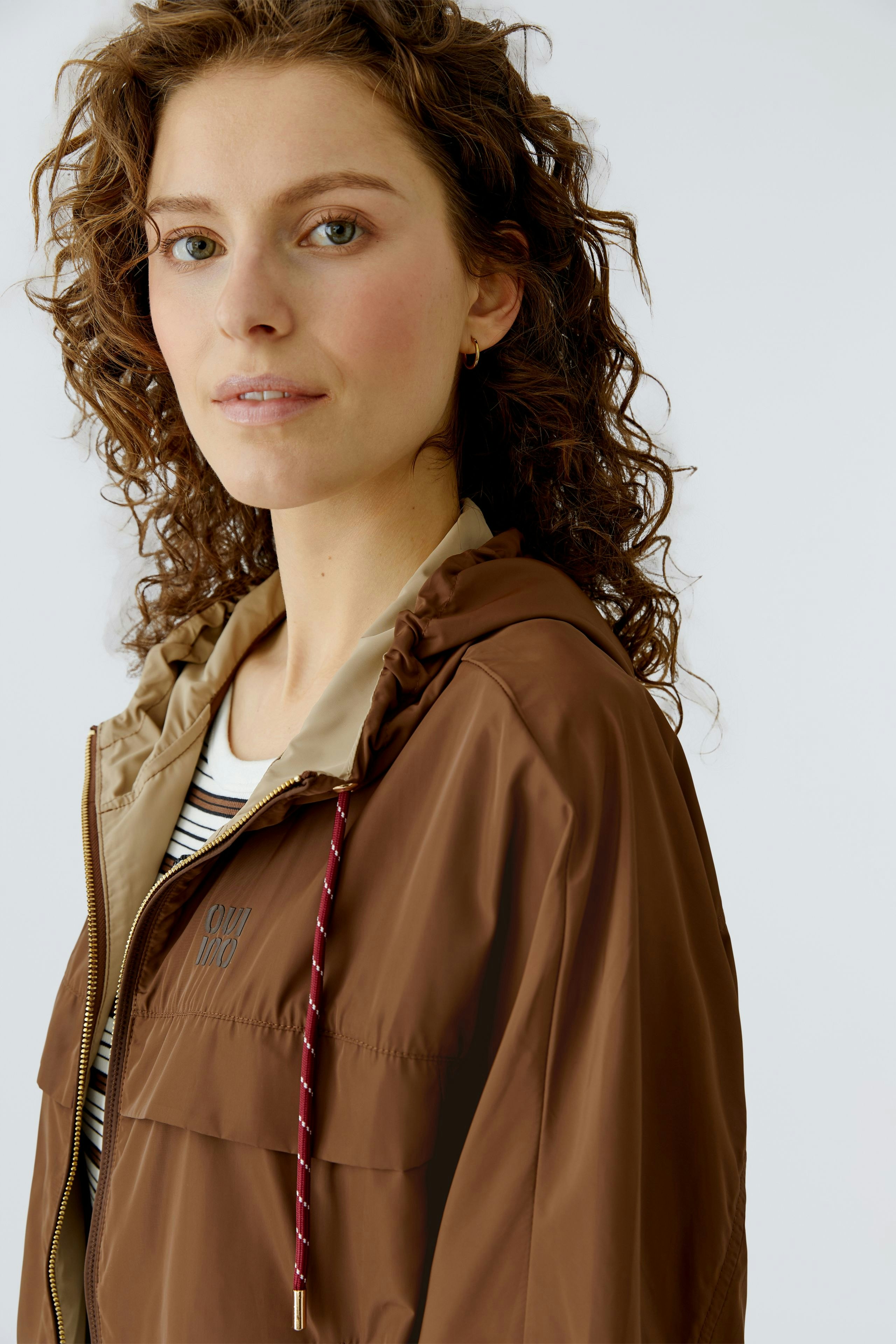 Bequeme Outdoorjacke: Frau in brauner Jacke mit Kapuze und sportlichem Look.