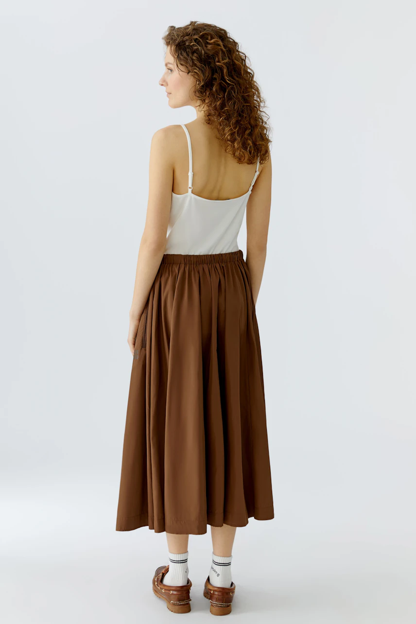 Casual A-line skirt: Woman in a brown A-line skirt with an elastic waistband, showcasing a relaxed style.