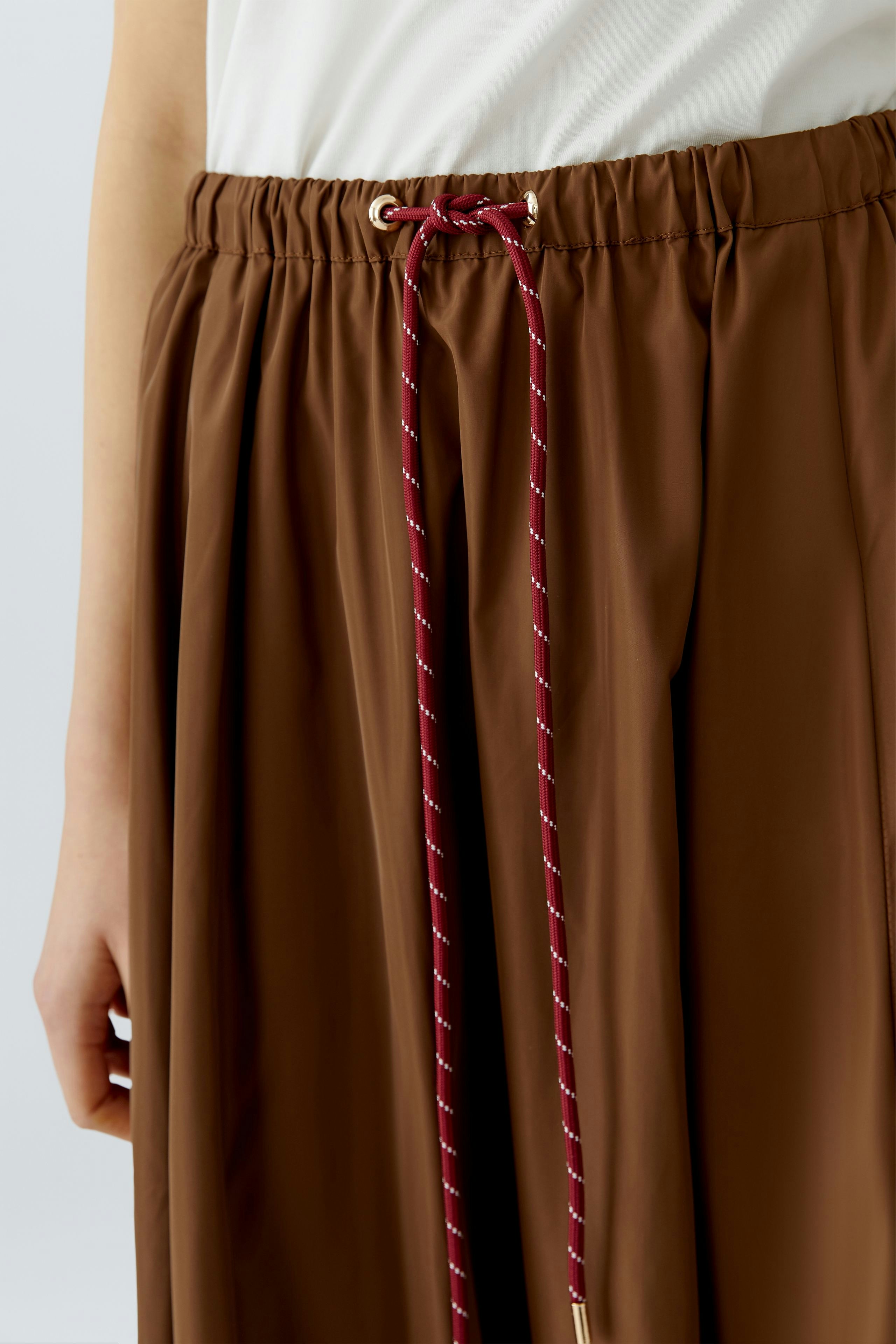 Casual A-line skirt: Woman wearing a brown A-line skirt with a drawstring waist for a relaxed look.