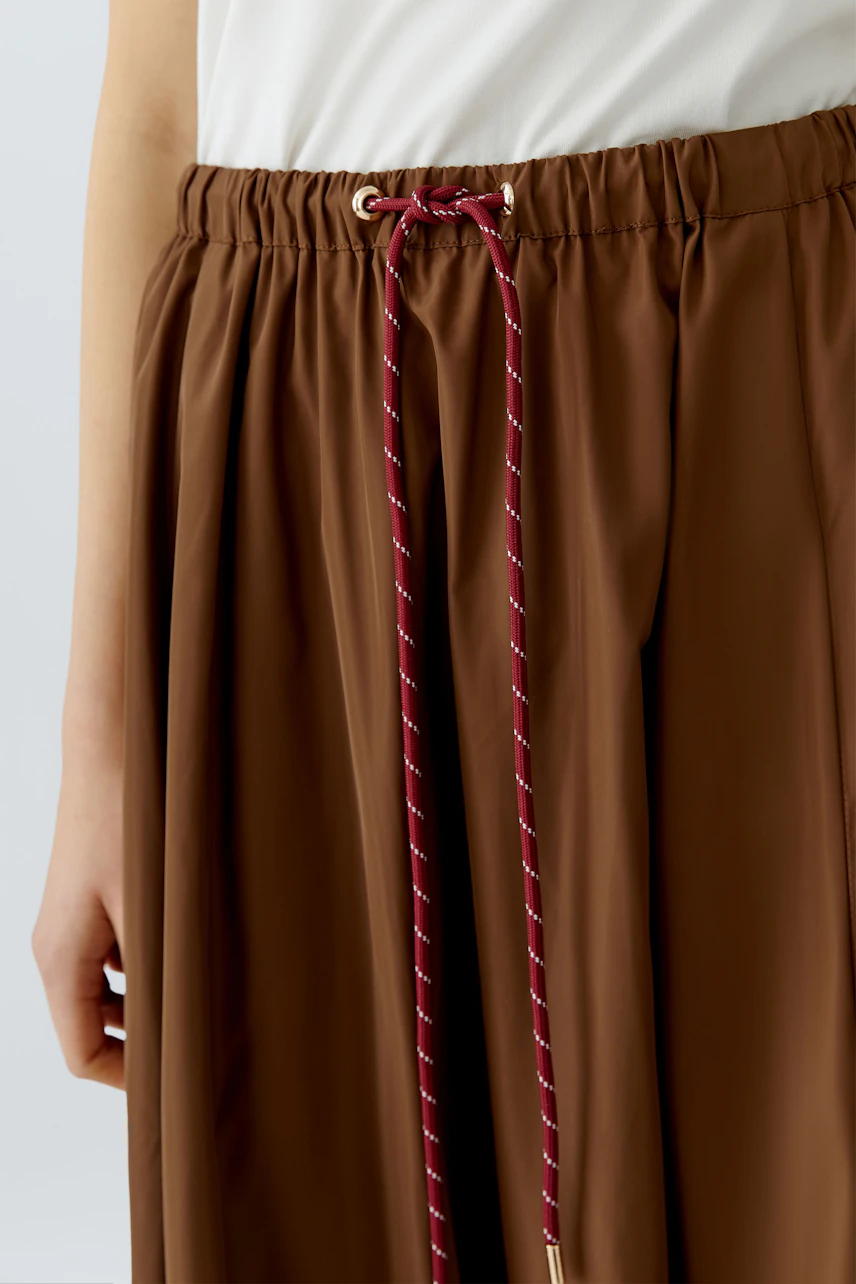 Casual A-line skirt: Woman wearing a brown A-line skirt with a drawstring waist for a relaxed look.