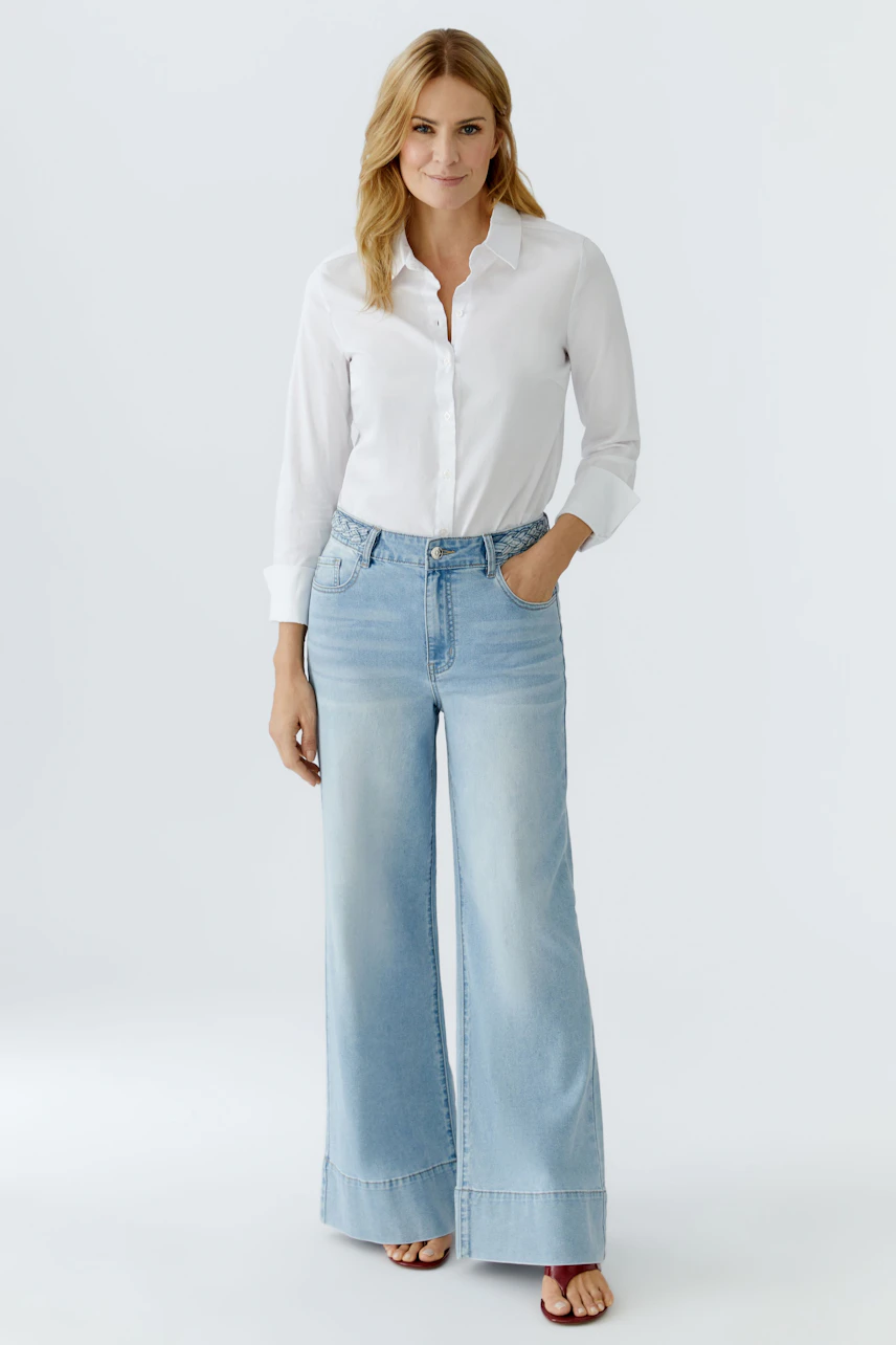 Wide leg jeans: Woman in light blue wide leg jeans paired with a white shirt, showcasing a relaxed style.