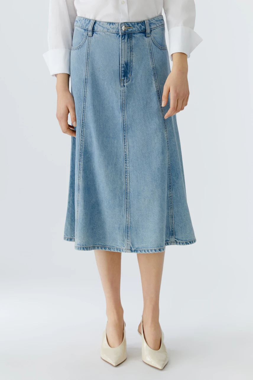 Casual denim skirt: Woman in a light blue jeans skirt paired with a white shirt, showcasing a relaxed style.