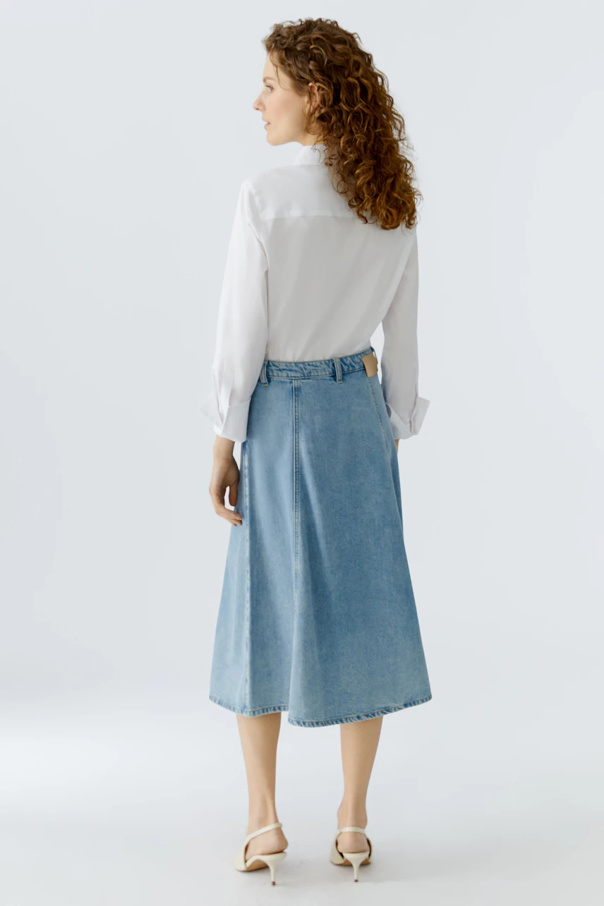 Casual denim skirt: Woman in a light blue jeans skirt paired with a white shirt, showcasing a relaxed style.
