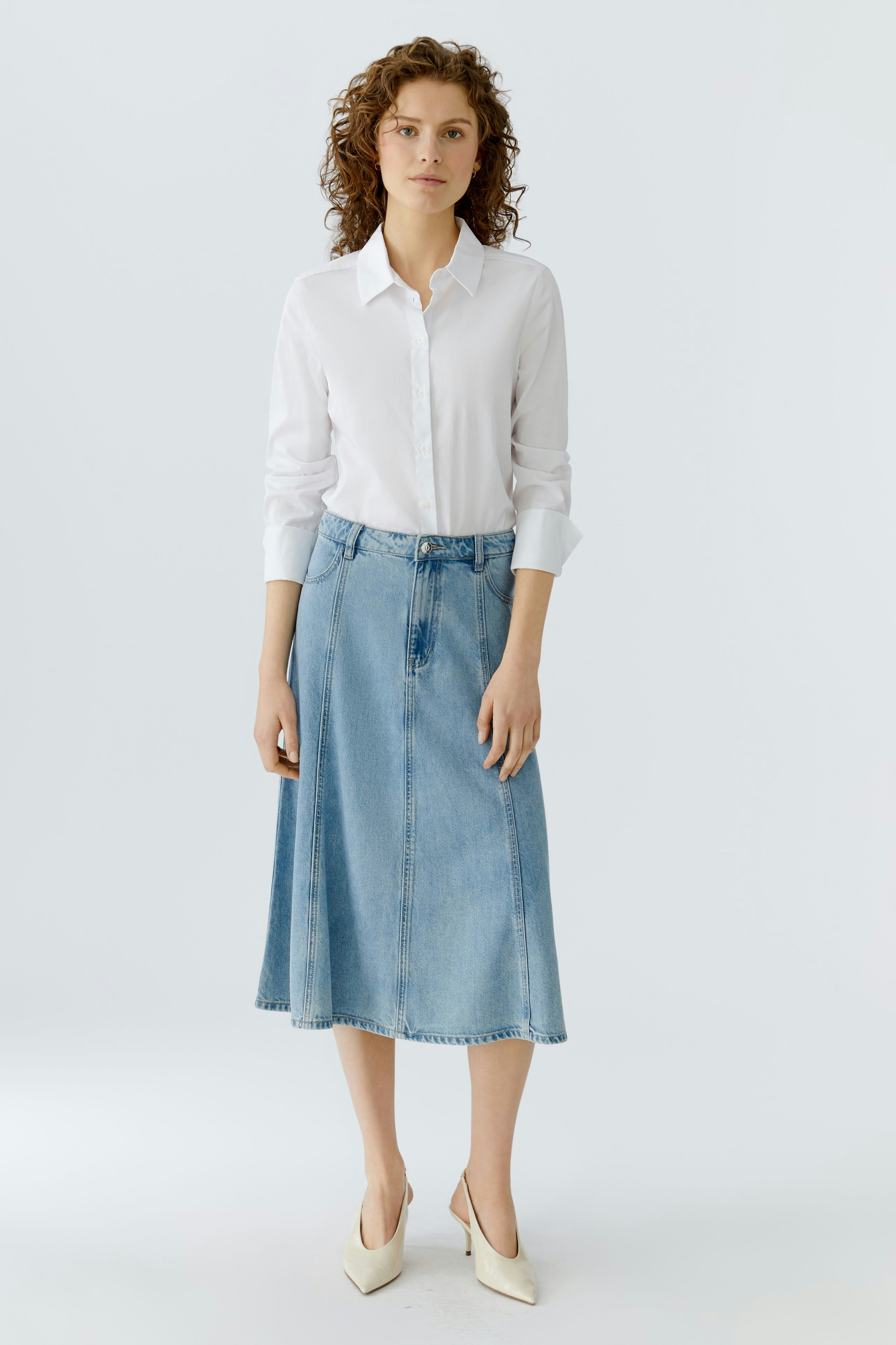 Damen Jeansrock: Frau in hellblauem Jeansrock und weißem Hemd steht lässig mit einem freundlichen Blick.