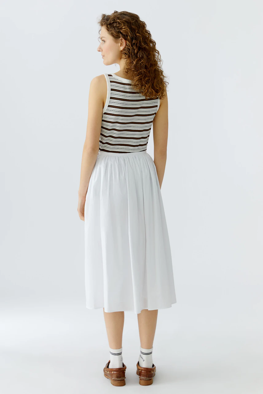 Casual A-line skirt: Woman in a white A-line skirt paired with a striped top, showcasing a relaxed style.