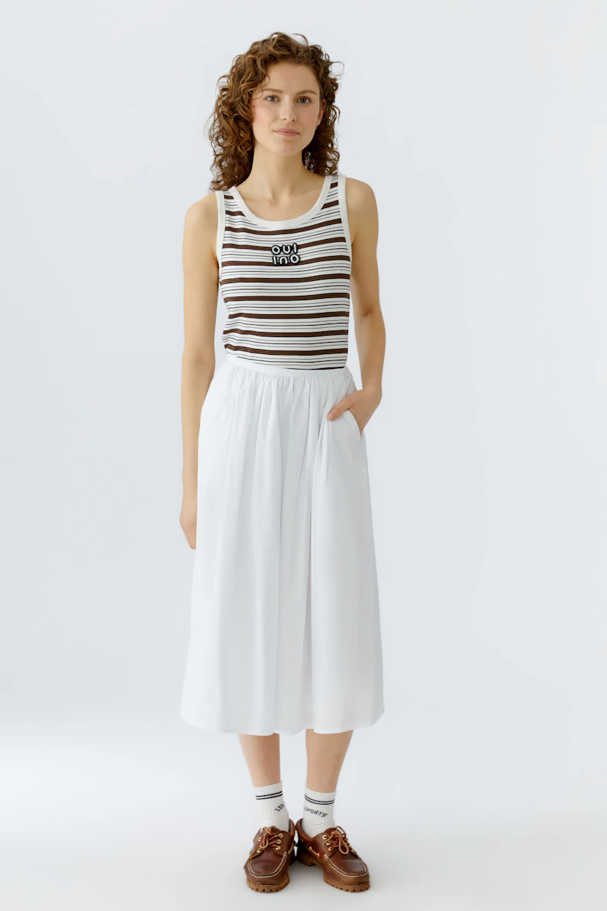 Casual A-line skirt: Woman in a white A-line skirt paired with a striped tank top and sporty shoes.