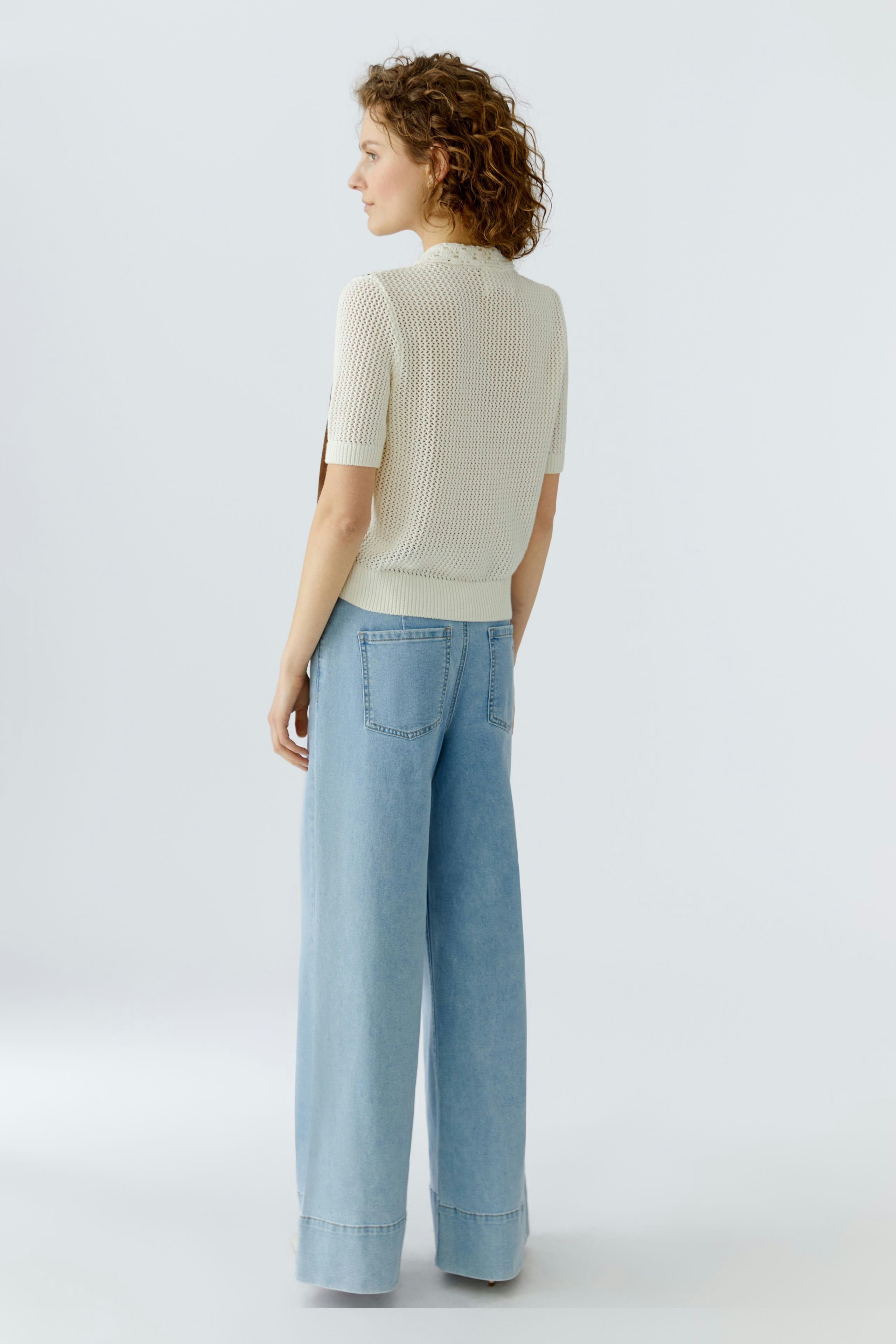 Casual women's cardigan: A woman in a light knit cardigan and wide jeans stands with her back to the camera.