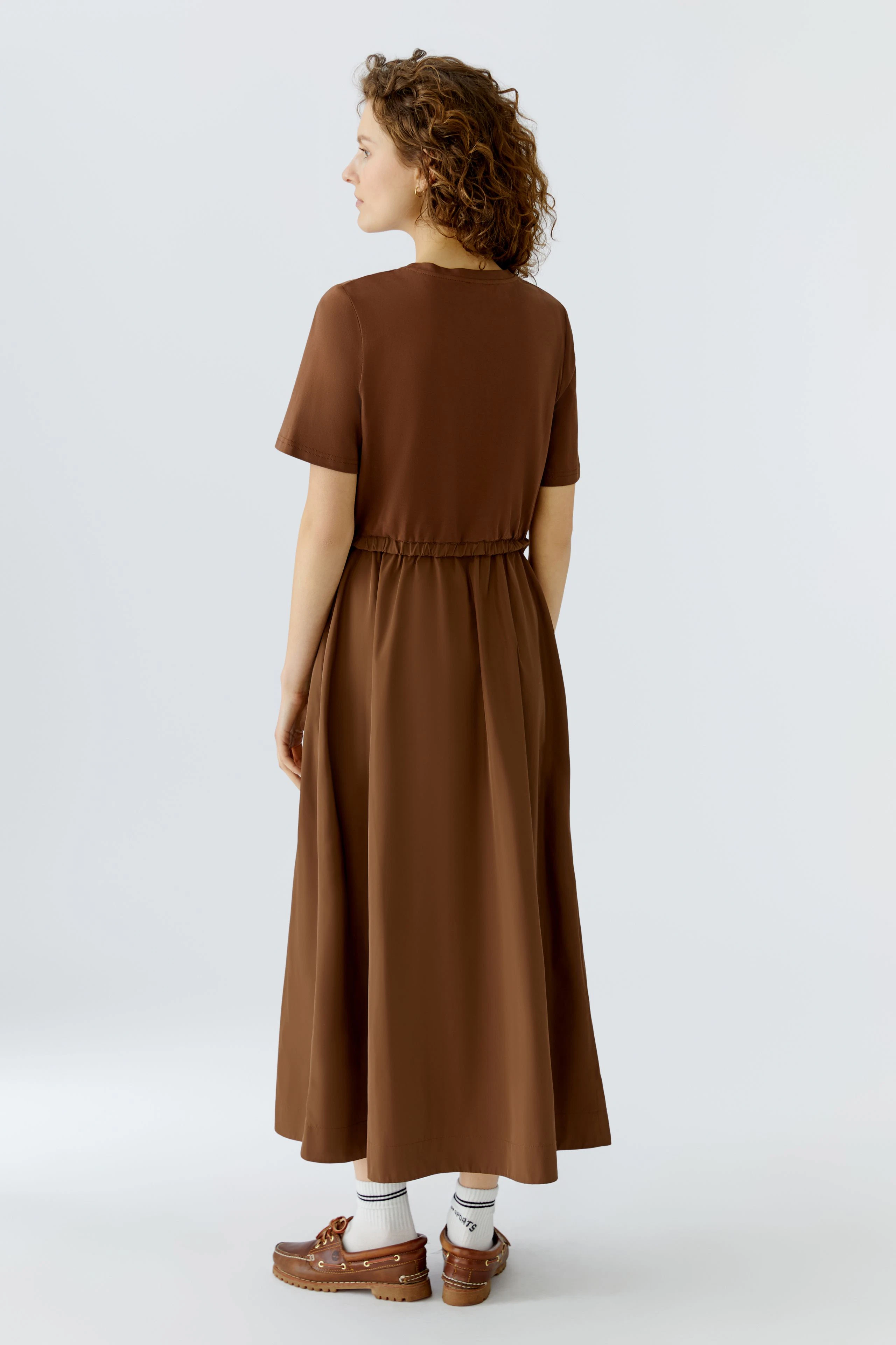 Bequemes Maxikleid: Frau mit lockigen Haaren trägt ein braunes Maxikleid mit kurzen Ärmeln und elastischem Bund.