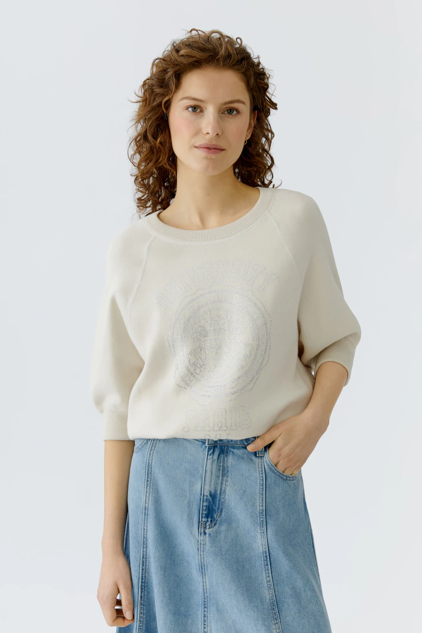 Casual women's pullover: Young woman in a light beige pullover with a graphic print, paired with a denim skirt.