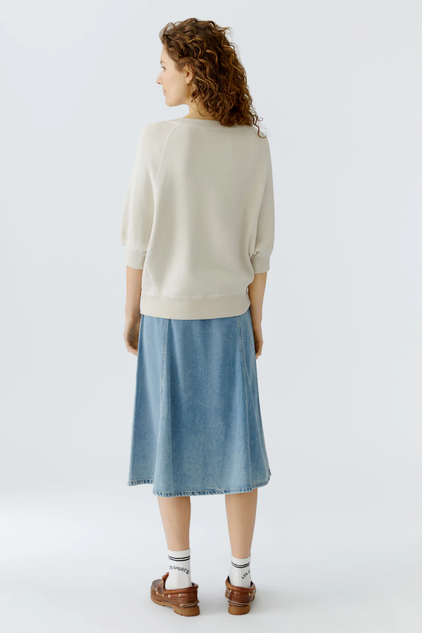 Casual women's pullover: A woman in a light pullover and denim skirt, showcasing a relaxed style.