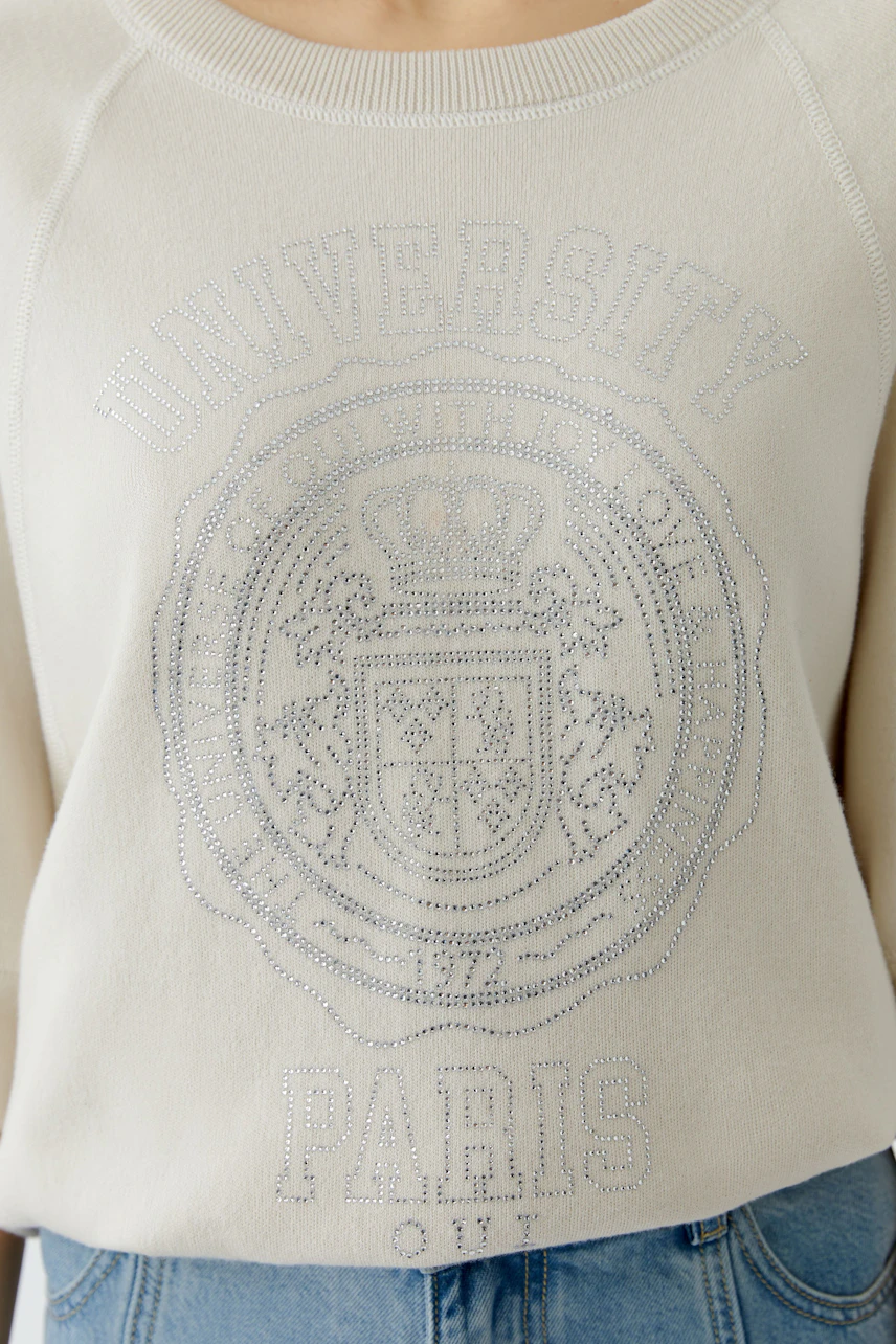 Casual women's pullover: A woman in a cream pullover with a university logo and relaxed fit.