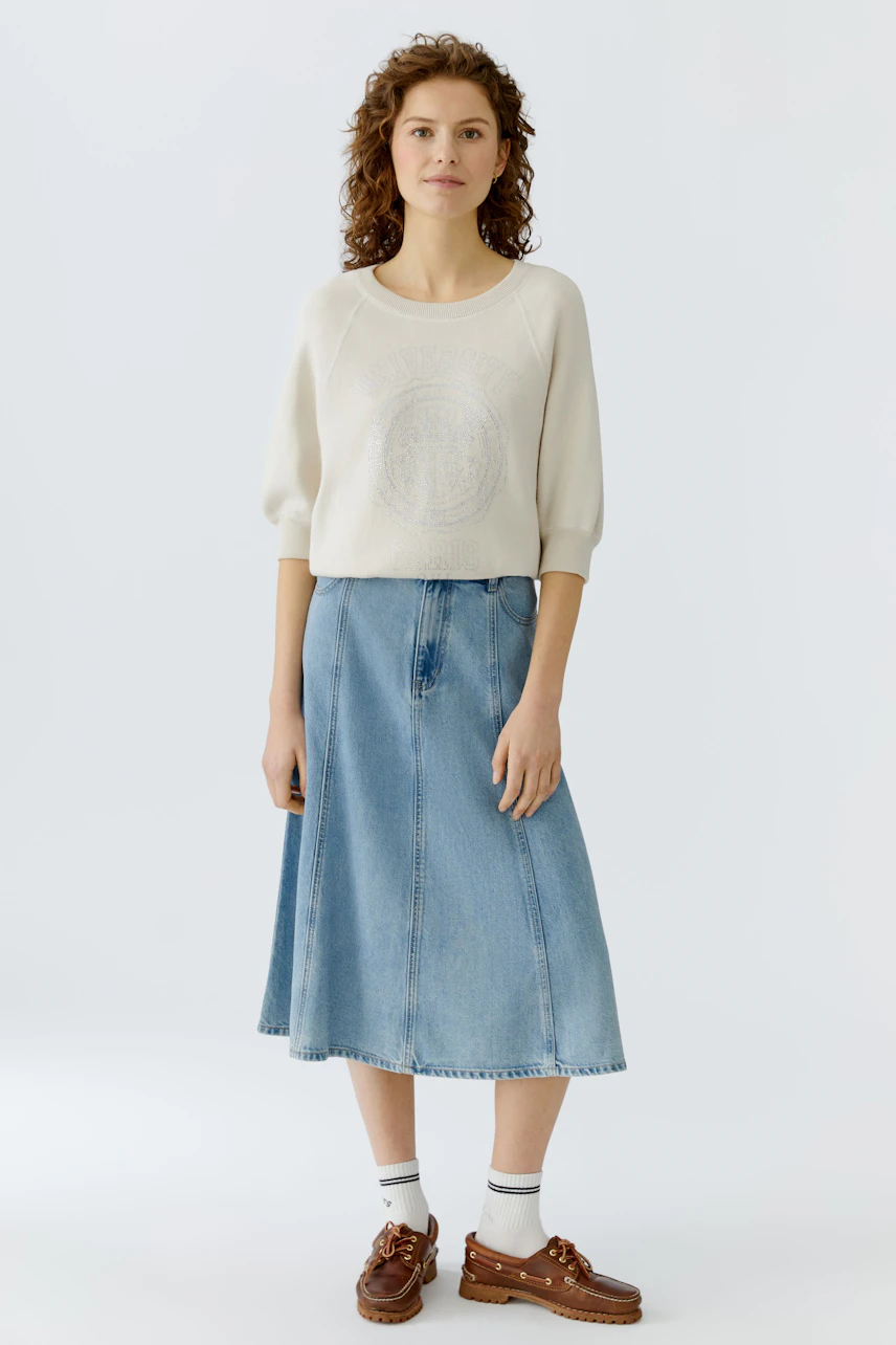 Casual women's pullover: Young woman in a cream pullover with a textured design and denim skirt.