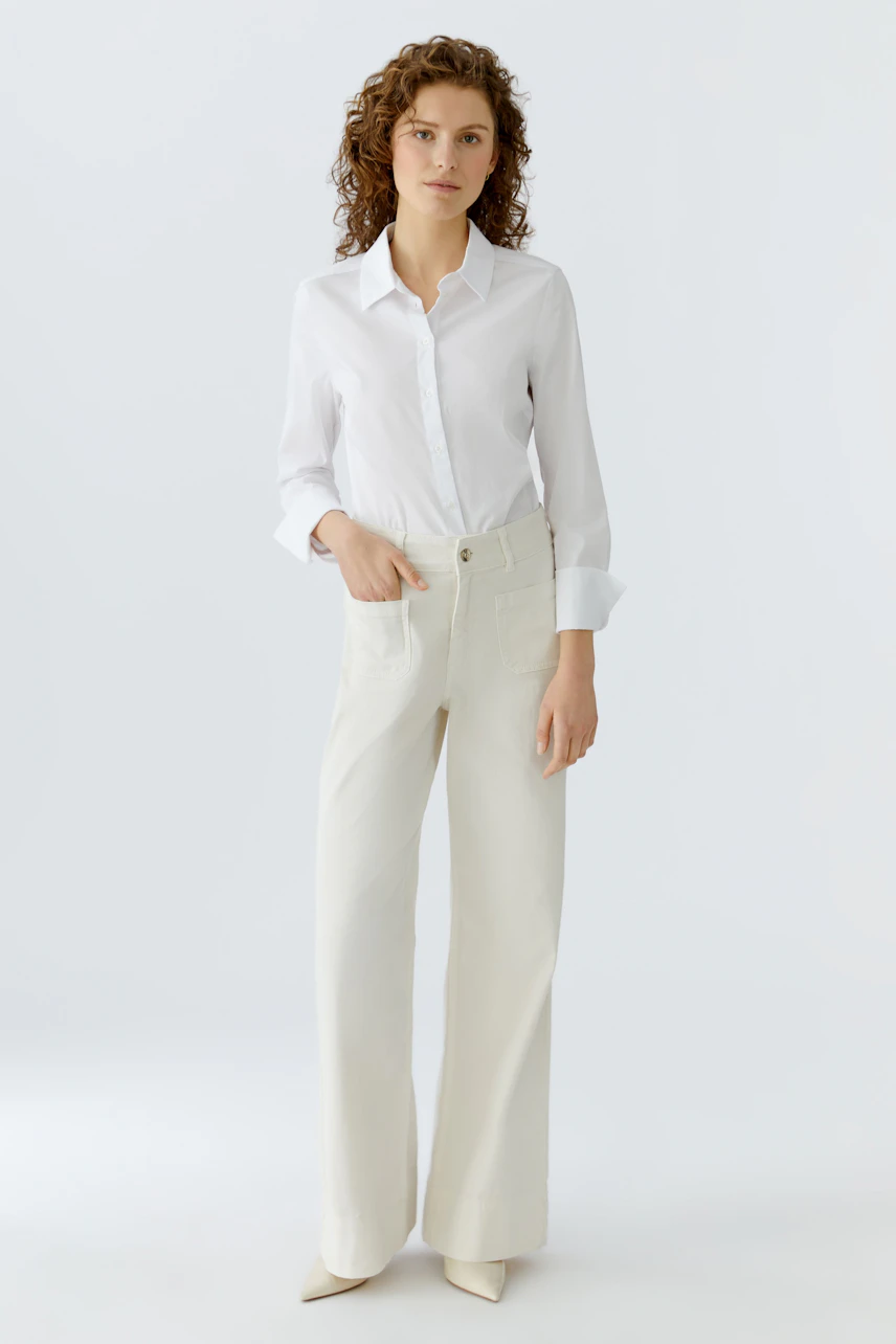 Wide leg jeans: A woman in a white shirt and cream wide leg jeans stands confidently.