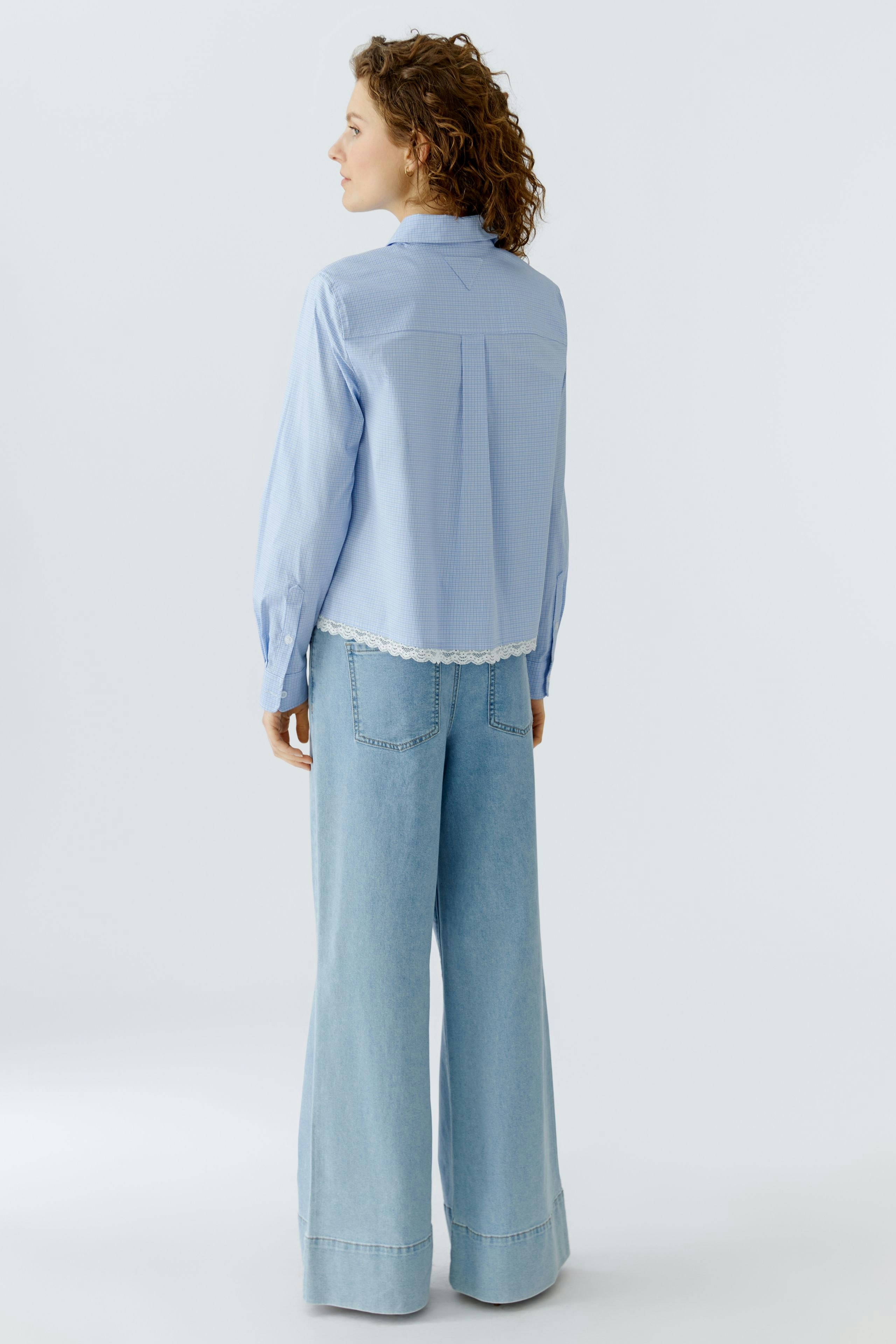 Hemdbluse: Frau trägt eine hellblaue Hemdbluse mit Rüschendetails und lässigen Jeans.