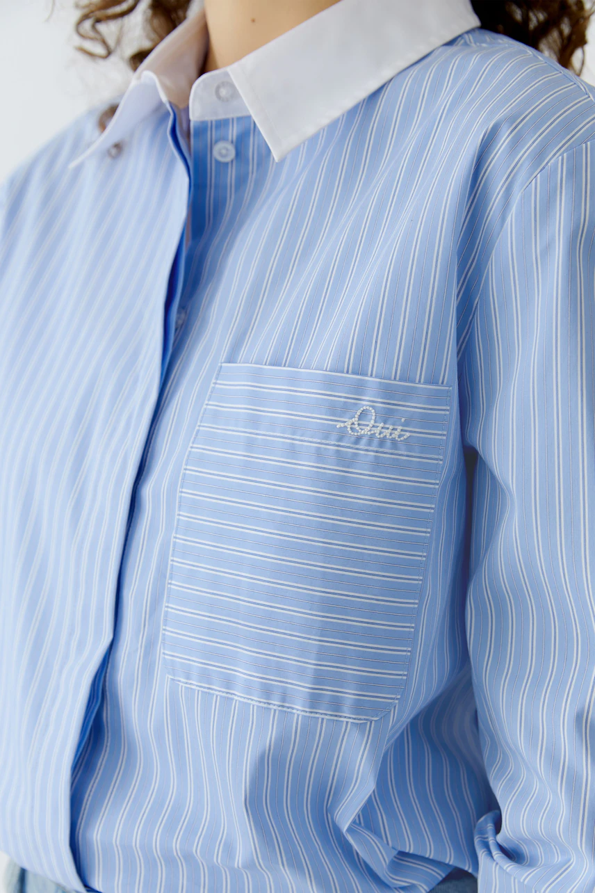 Casual women's blouse: A woman in a light blue striped blouse with a white collar and pocket detail.