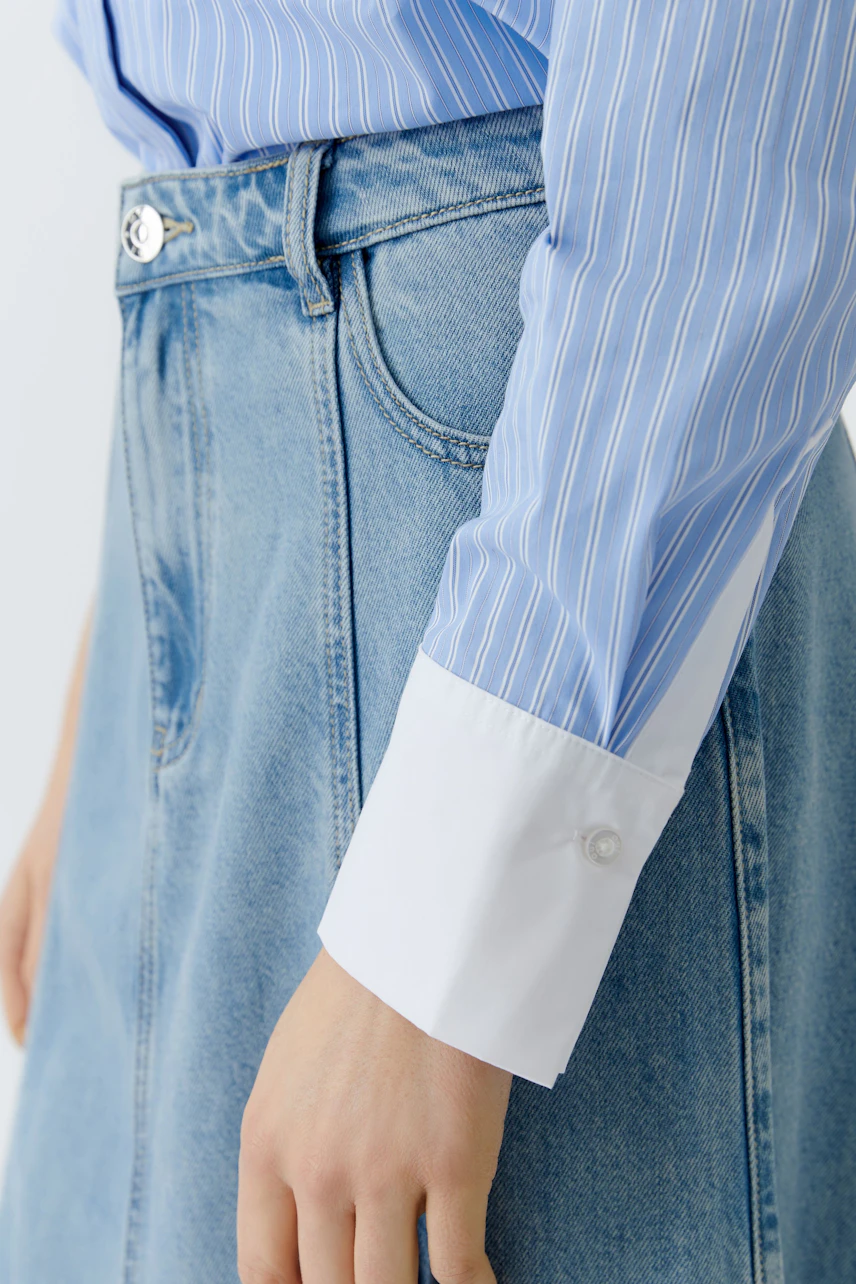 Stylish women's blouse: Close-up of a woman wearing a blue striped blouse with white cuffs.