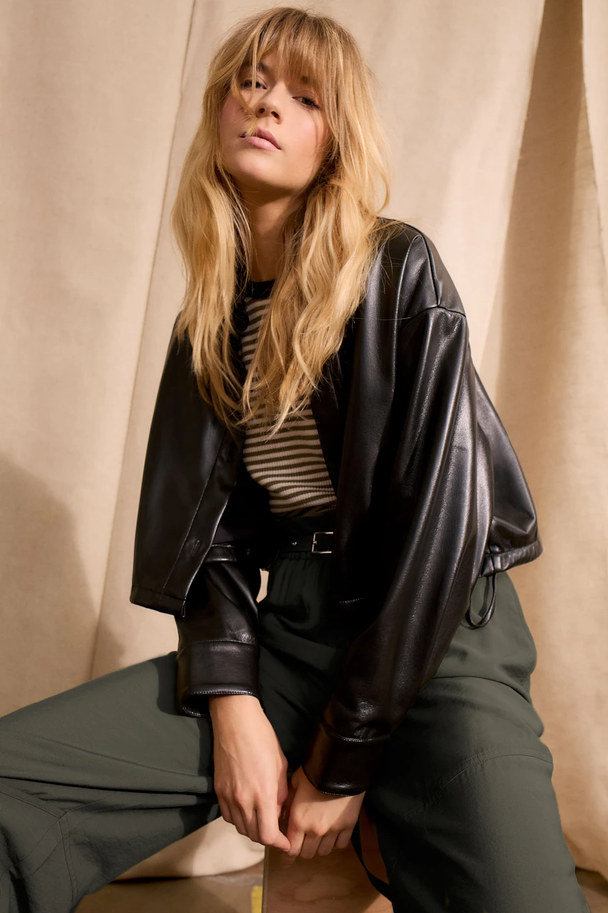 Casual women's pullover: Young woman in a striped pullover and leather jacket poses confidently.