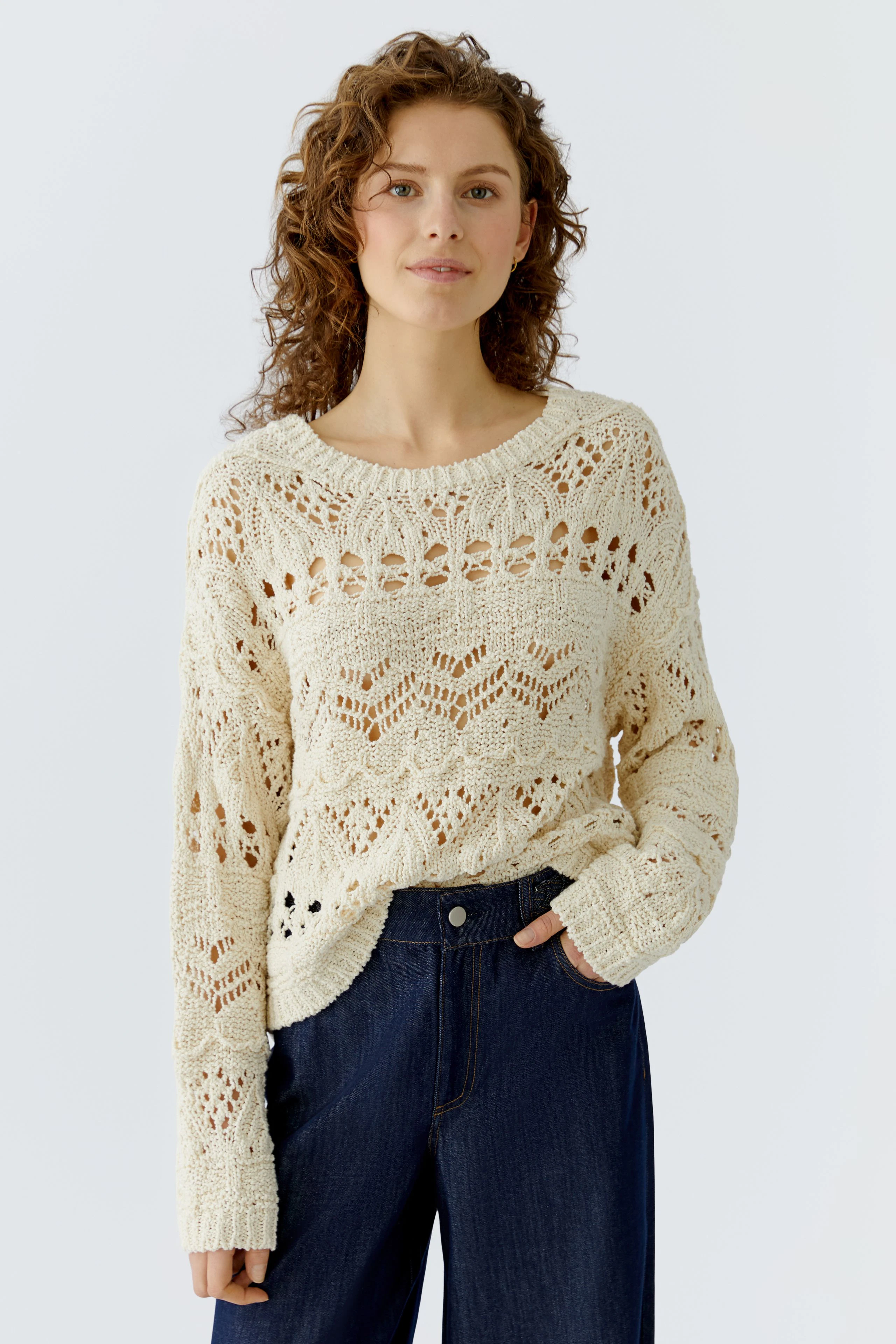 Damen-Pullover: Junge Frau in einem hellen, luftigen Strickpullover mit Lochmuster und lässiger Jeans.