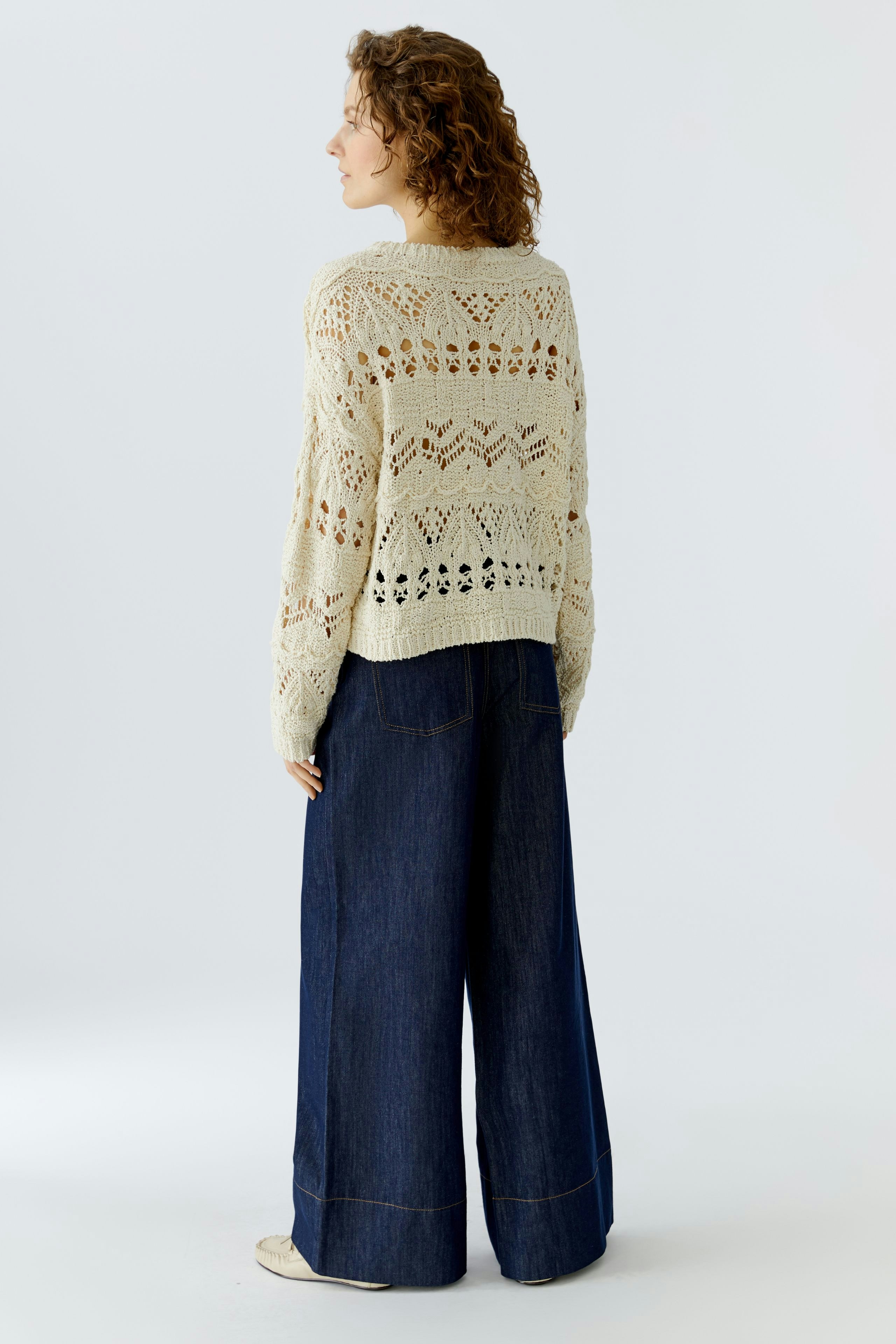 Casual women's pullover: A woman in a light knitted pullover with an open pattern and wide jeans.