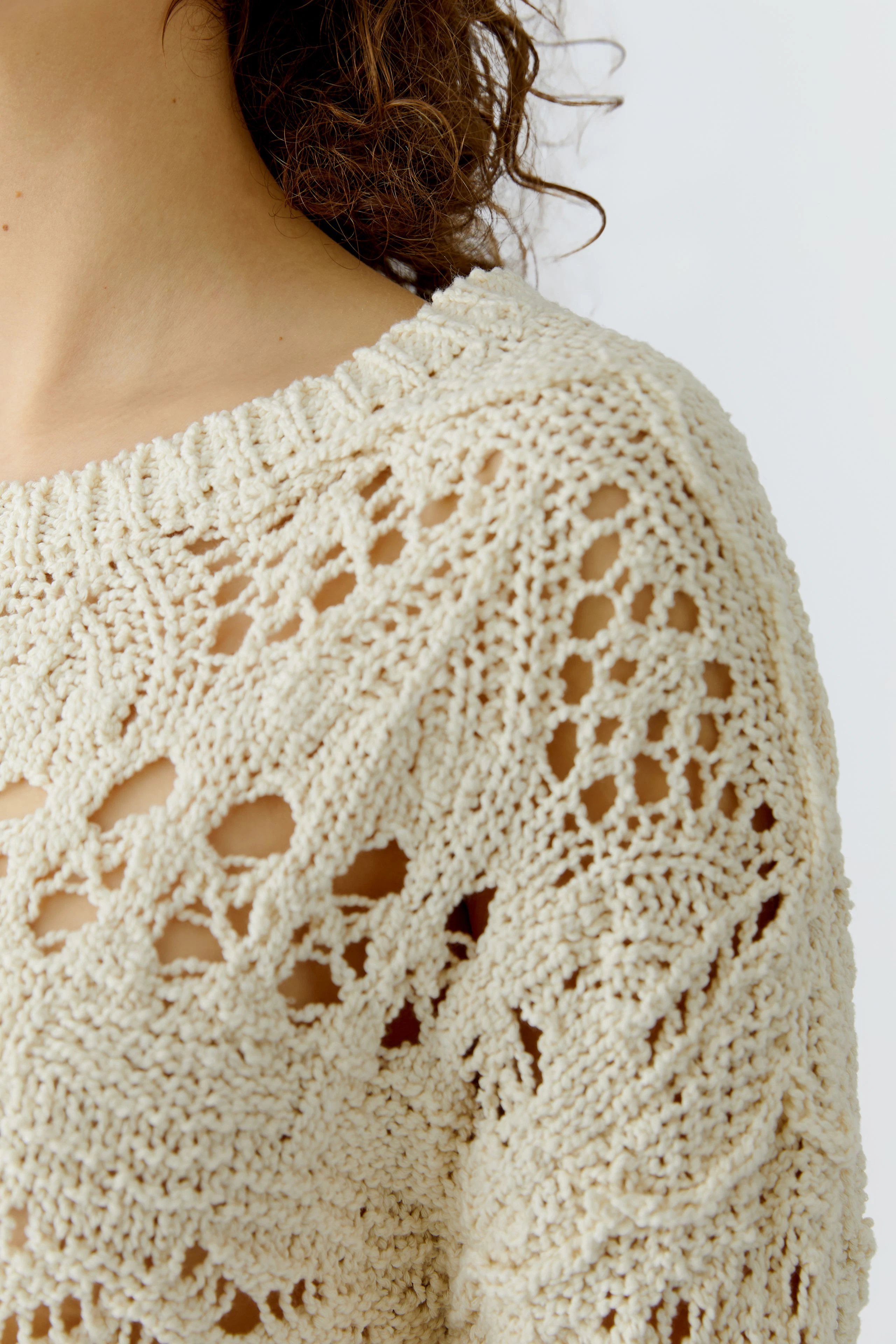 Damen-Pullover: Frau trägt einen hellen, grob gestrickten Pullover mit einem offenen Muster.