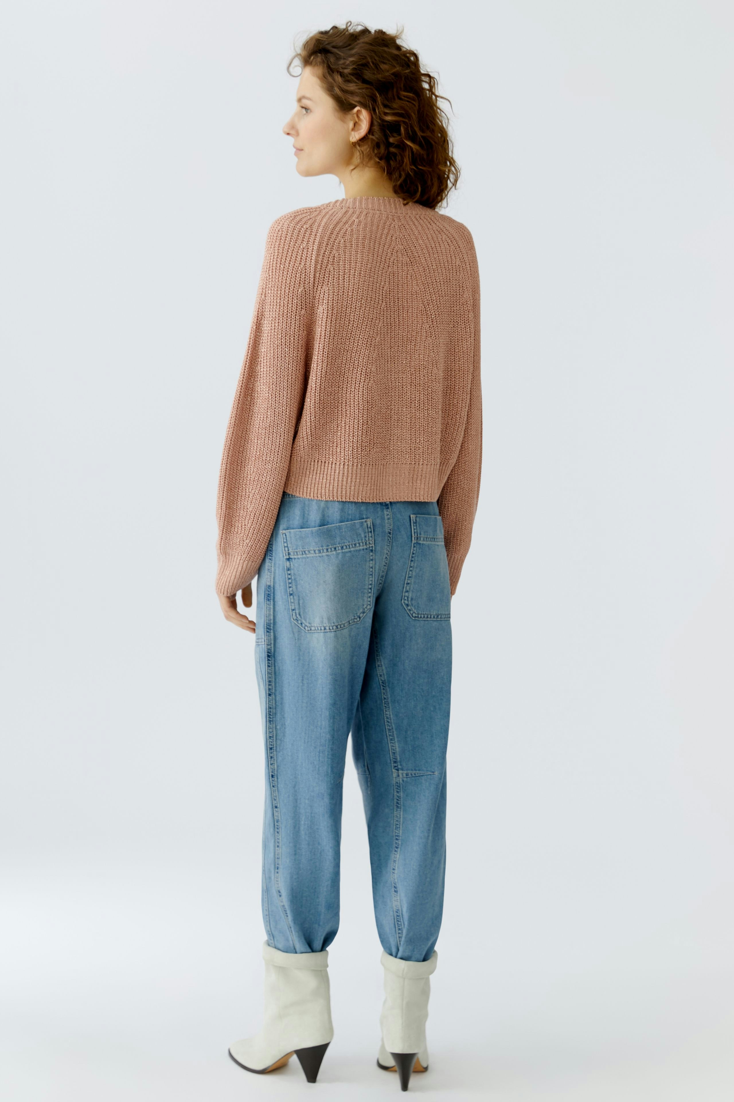 Casual women's cardigan: A woman in a cropped, ribbed pink cardigan paired with relaxed jeans.