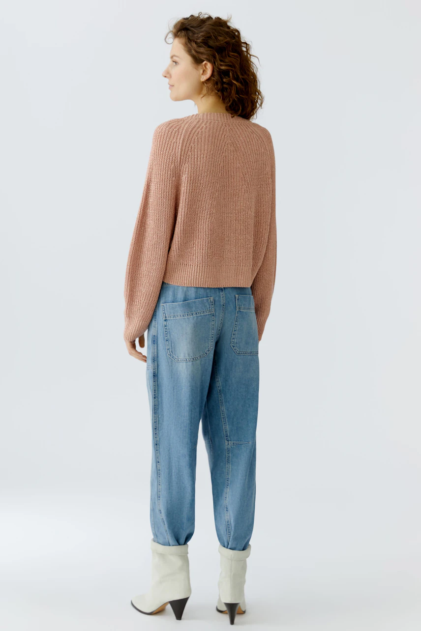 Casual women's cardigan: A woman in a cropped, ribbed pink cardigan paired with relaxed jeans.