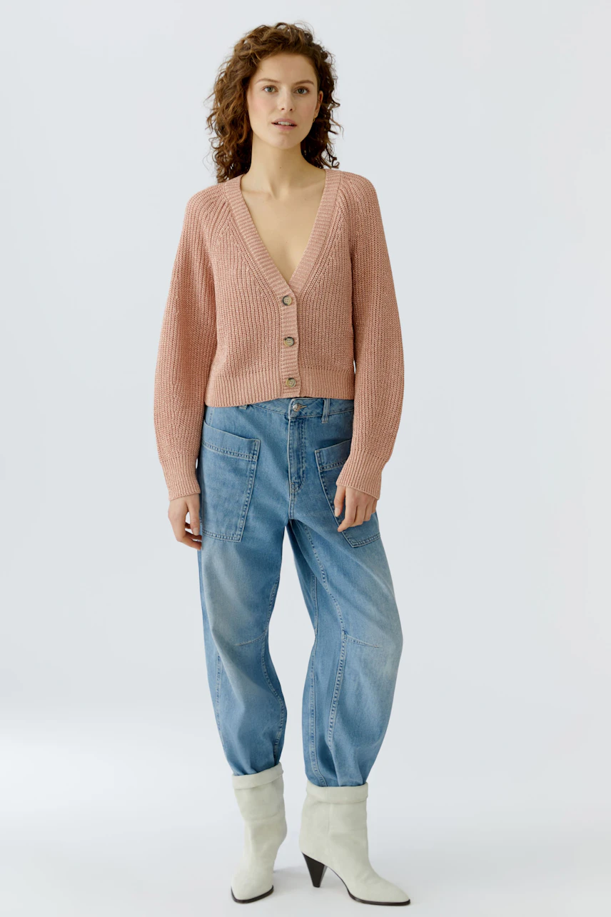 Casual women's cardigan: A woman in a pink knitted cardigan with buttons and relaxed-fit jeans.