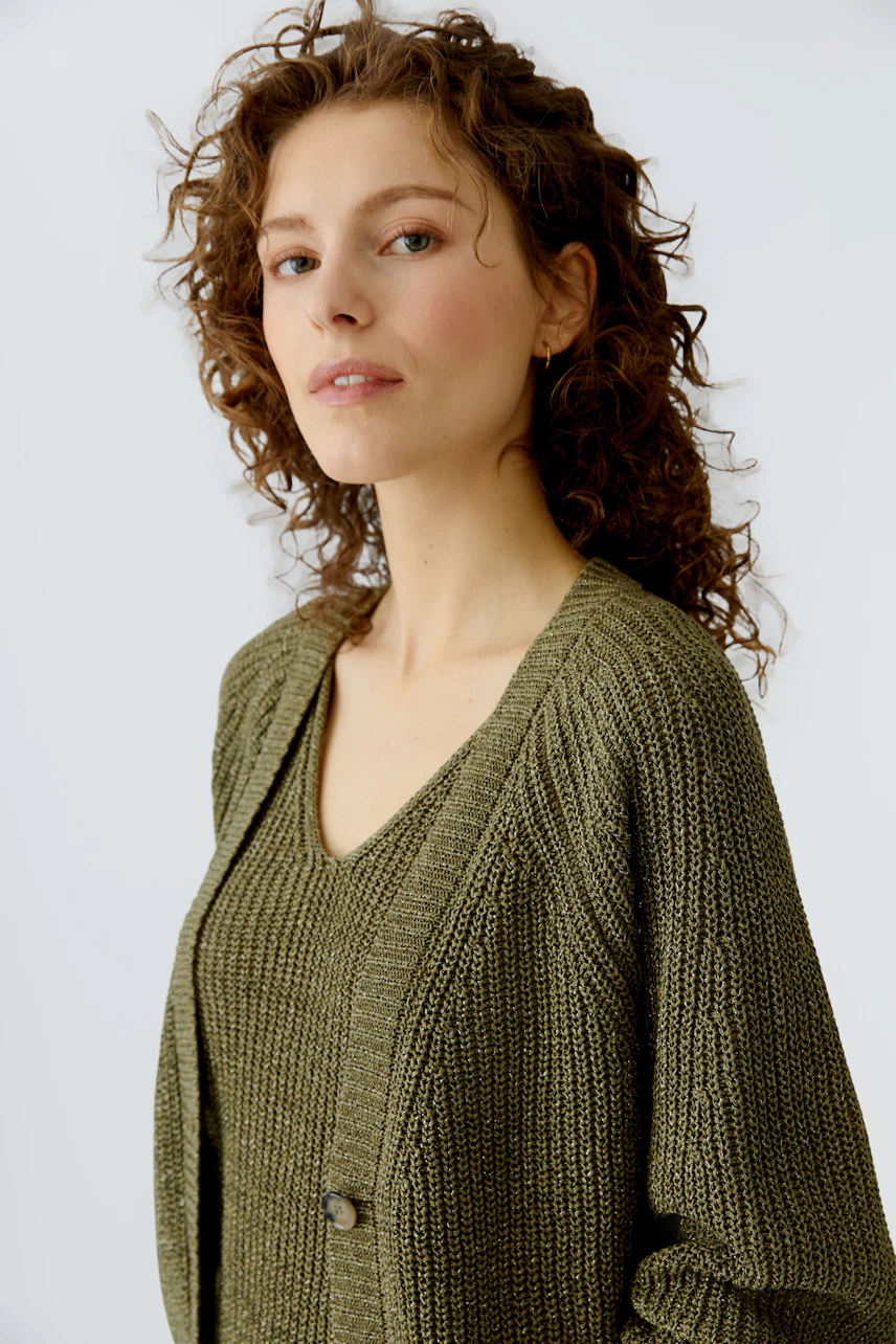 Damen-Strickjacke: Frau mit lockigen Haaren trägt eine olivgrüne Strickjacke mit V-Ausschnitt.