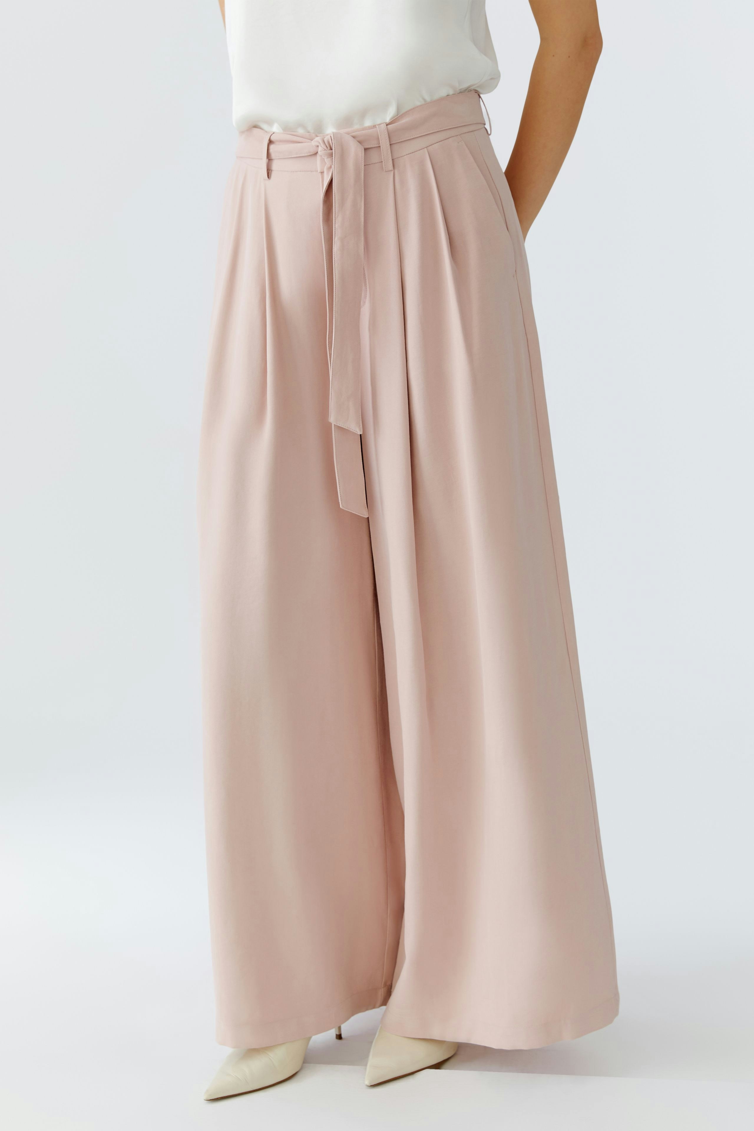 Wide-leg trousers: A woman in soft pink pleated trousers with a tied waist, perfect for casual wear.