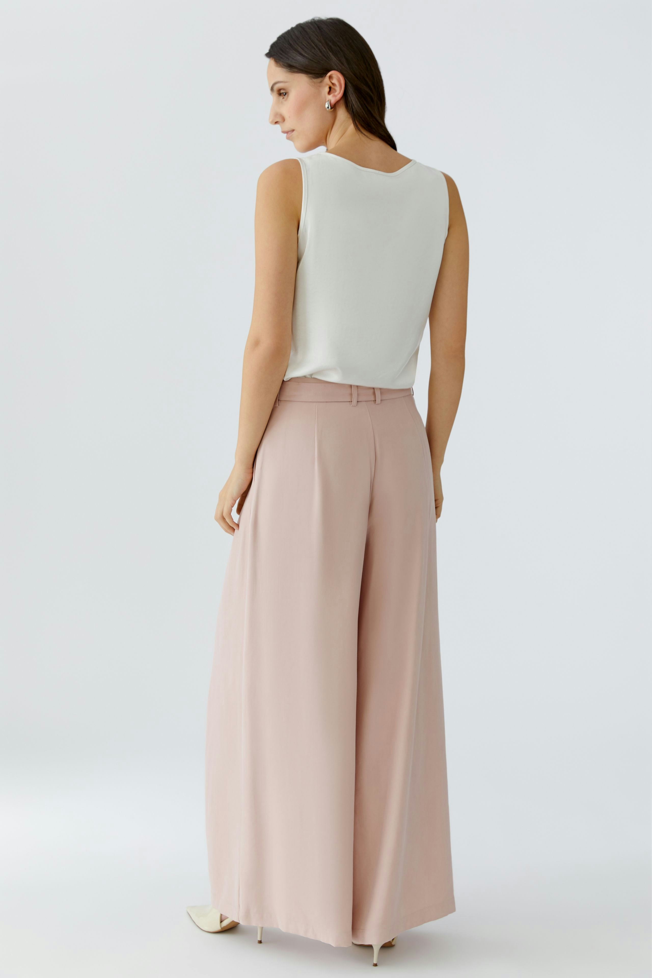 Wide-leg trousers: Woman in light pink pleated pants, showcasing a relaxed and modern style.
