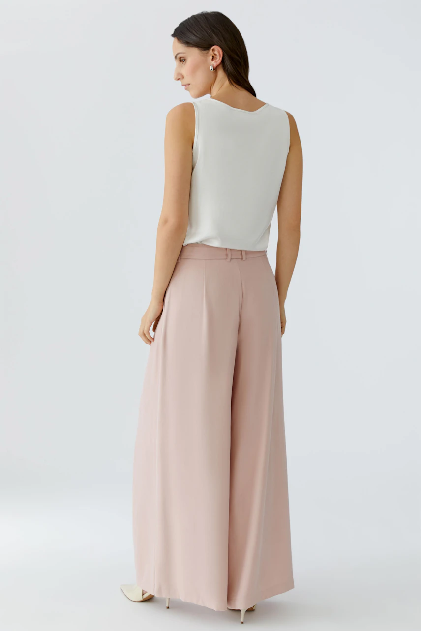 Bundfaltenhose: Frau trägt eine weite, rosa Hose mit Bundfalten und einem schlichten, weißen Oberteil.