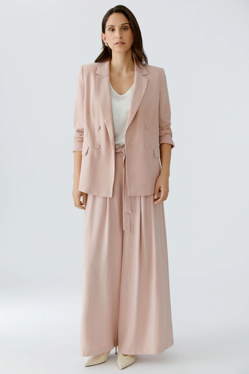 Moderne Bundfaltenhose: Frau in bequemer, weit geschnittener Hose in zartem Rosa mit passendem Blazer.