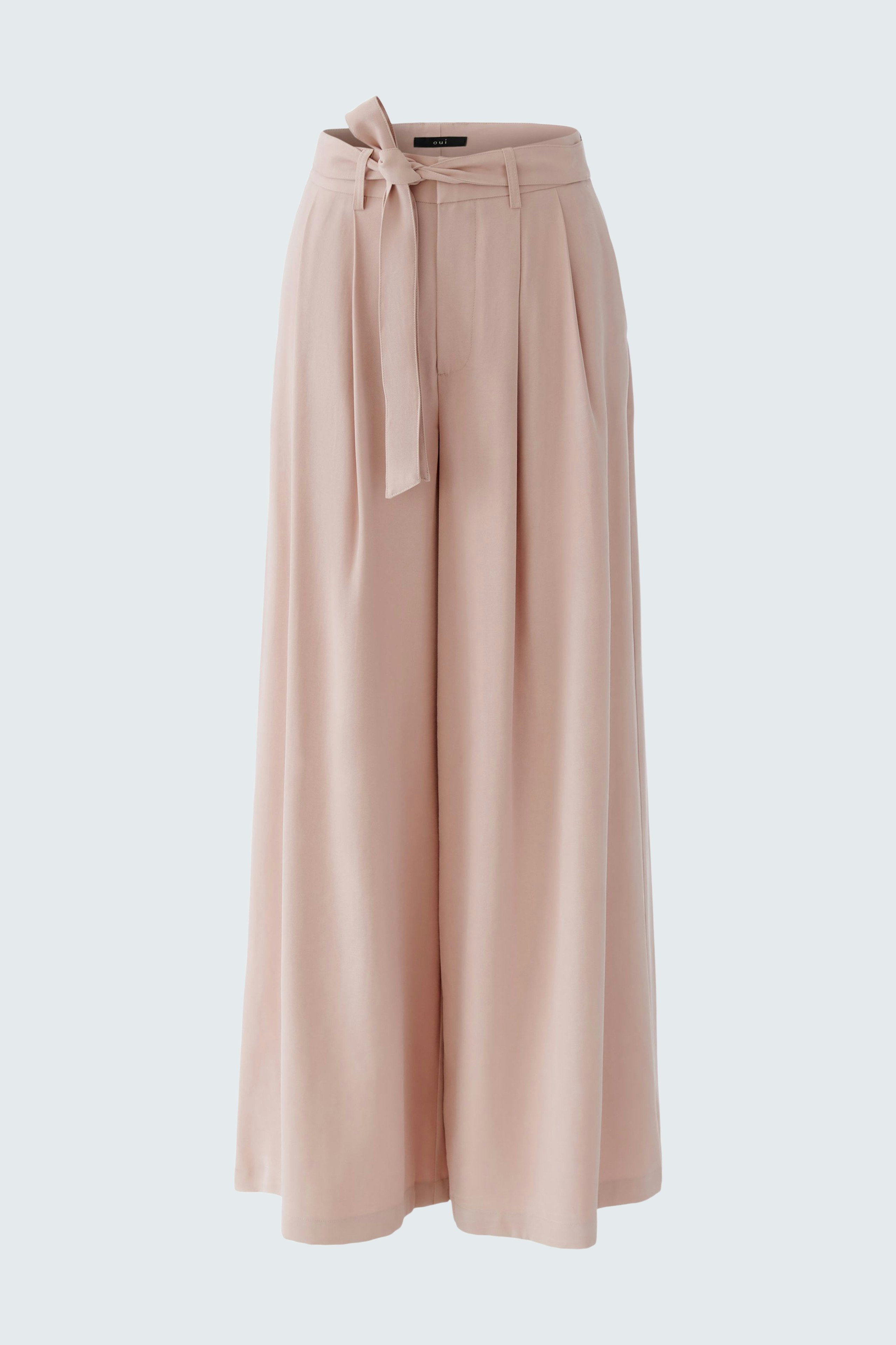 Wide-leg trousers: A woman in soft pink pleated trousers with a tie belt, showcasing a relaxed style.