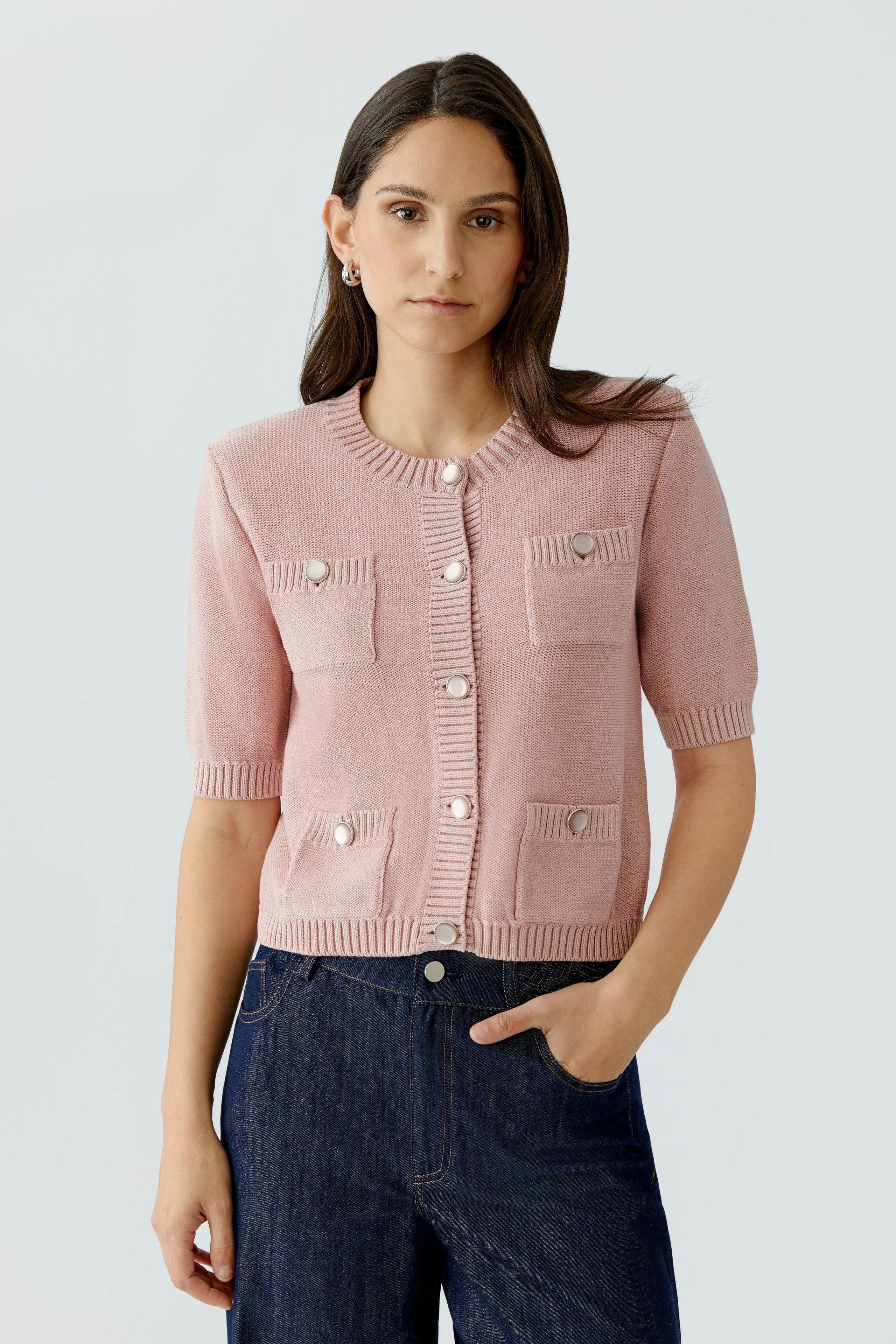 Casual women's cardigan: Young woman in a pink cardigan with pockets and buttons, paired with jeans.