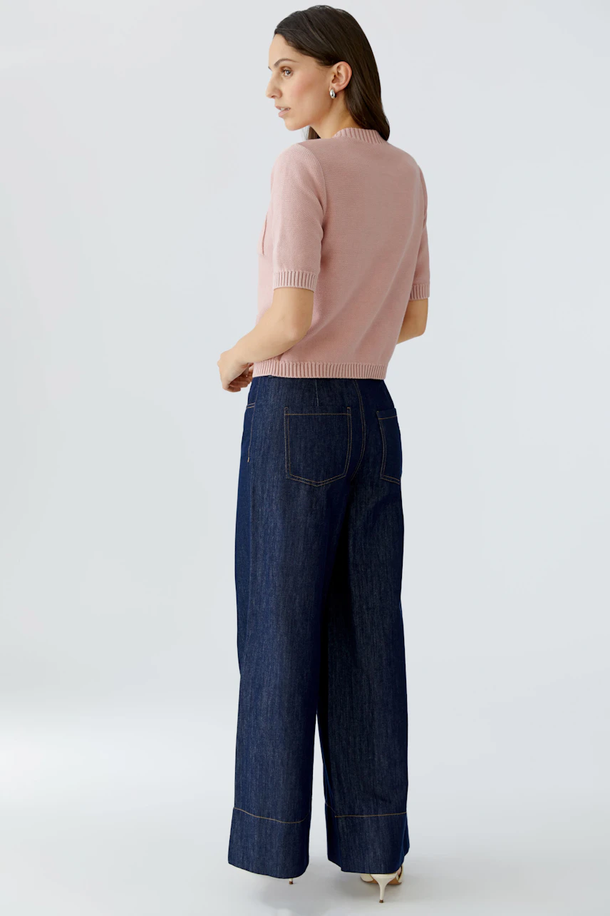 Damen-Strickjacke: Frau in rosa Strickjacke mit kurzen Ärmeln und lässigen Jeans, von hinten zu sehen.