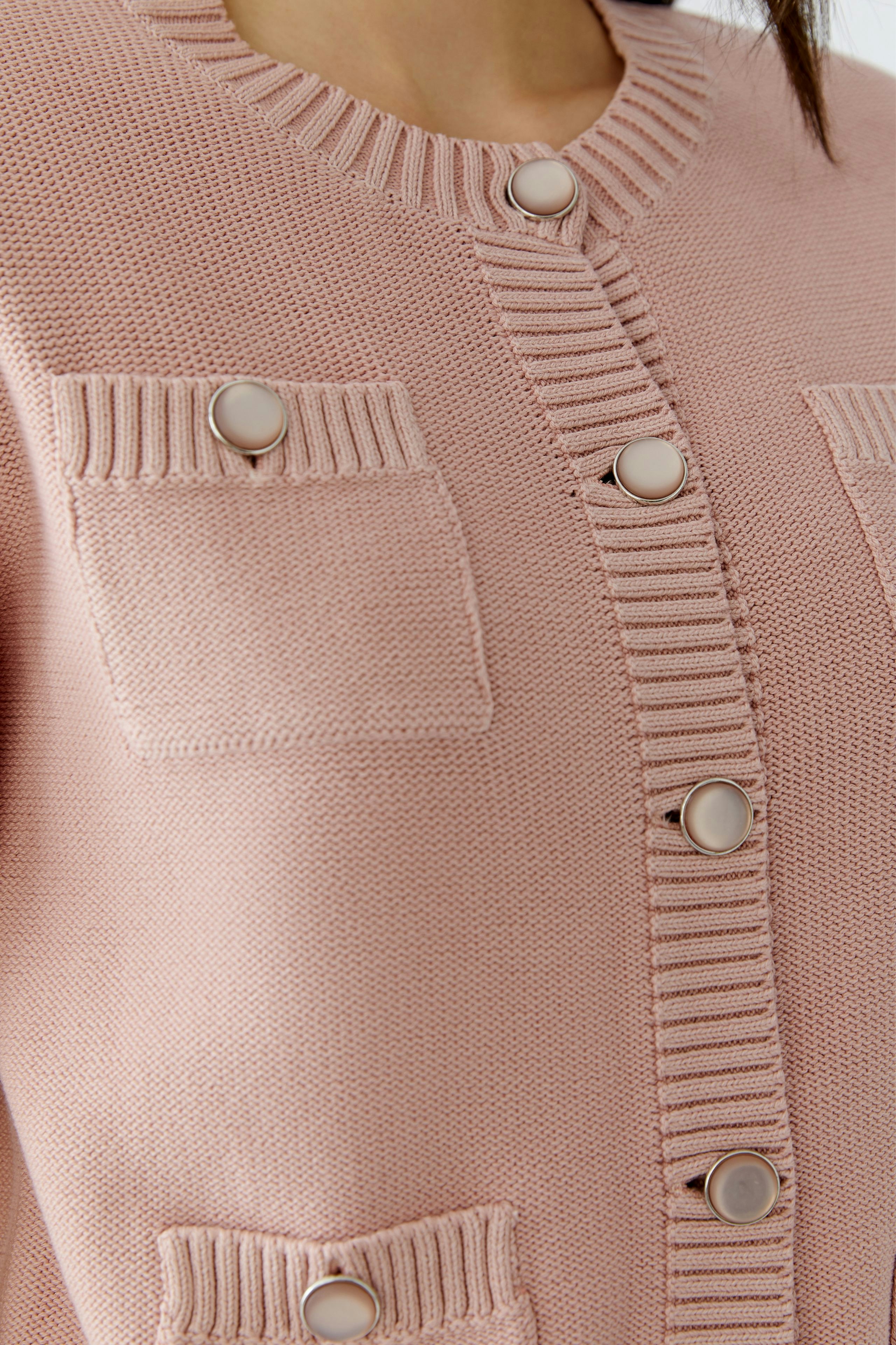 Casual women's cardigan: Close-up of a woman in a pink knitted cardigan with pockets and buttons.