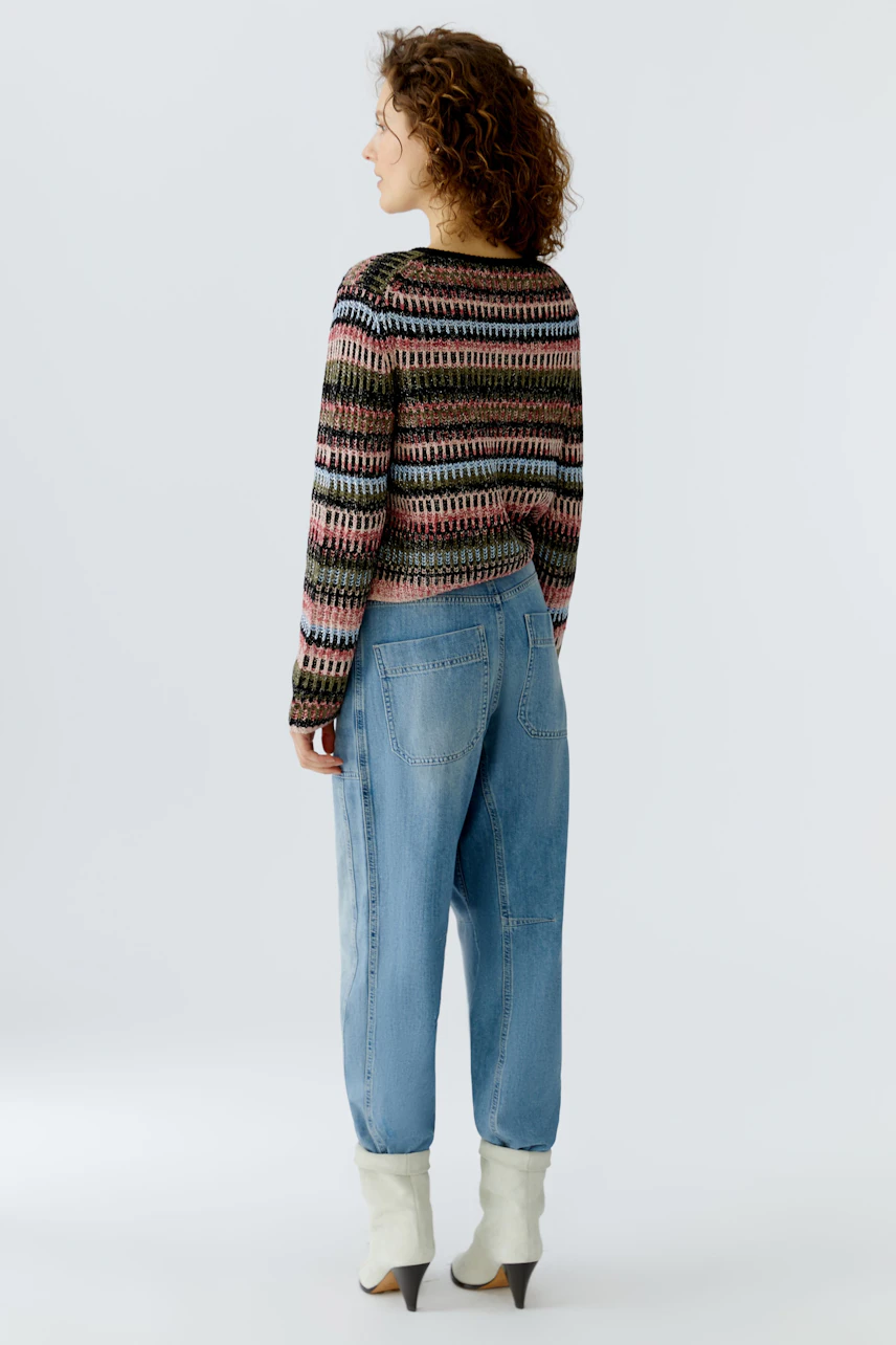 Bunte Damen-Strickjacke: Frau mit lockigen Haaren trägt eine farbenfrohe Strickjacke und lässige Jeans.