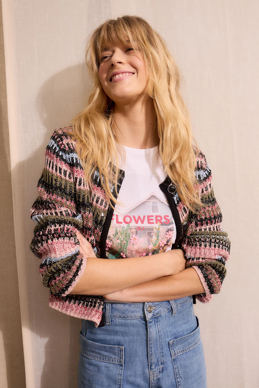 Bunte Damen-Strickjacke: Frau mit lässigem Outfit lächelt, trägt eine farbenfrohe Strickjacke.