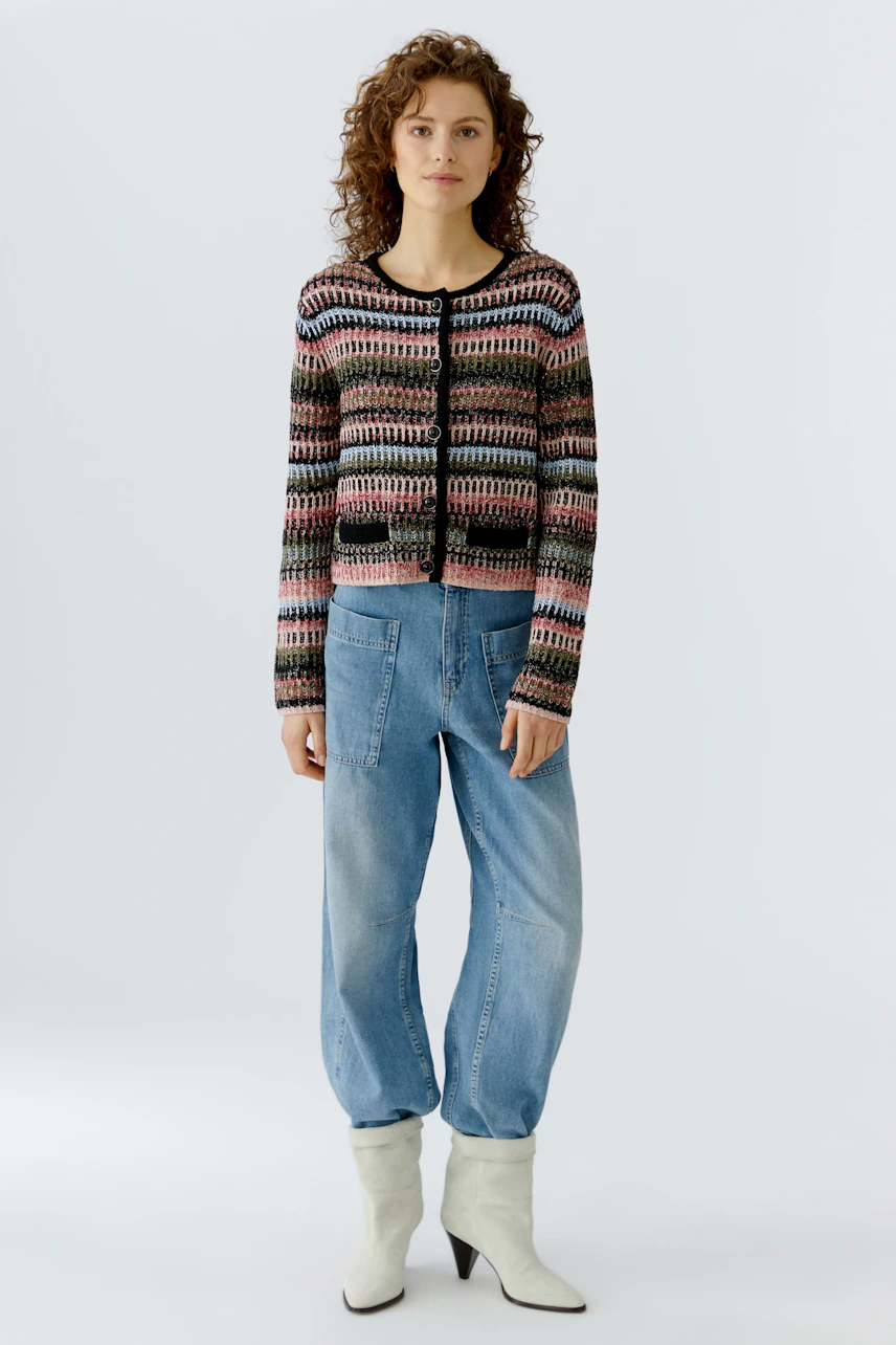 Bunte Damen-Strickjacke: Frau trägt eine farbenfrohe Strickjacke mit Muster und lässigen Jeans.