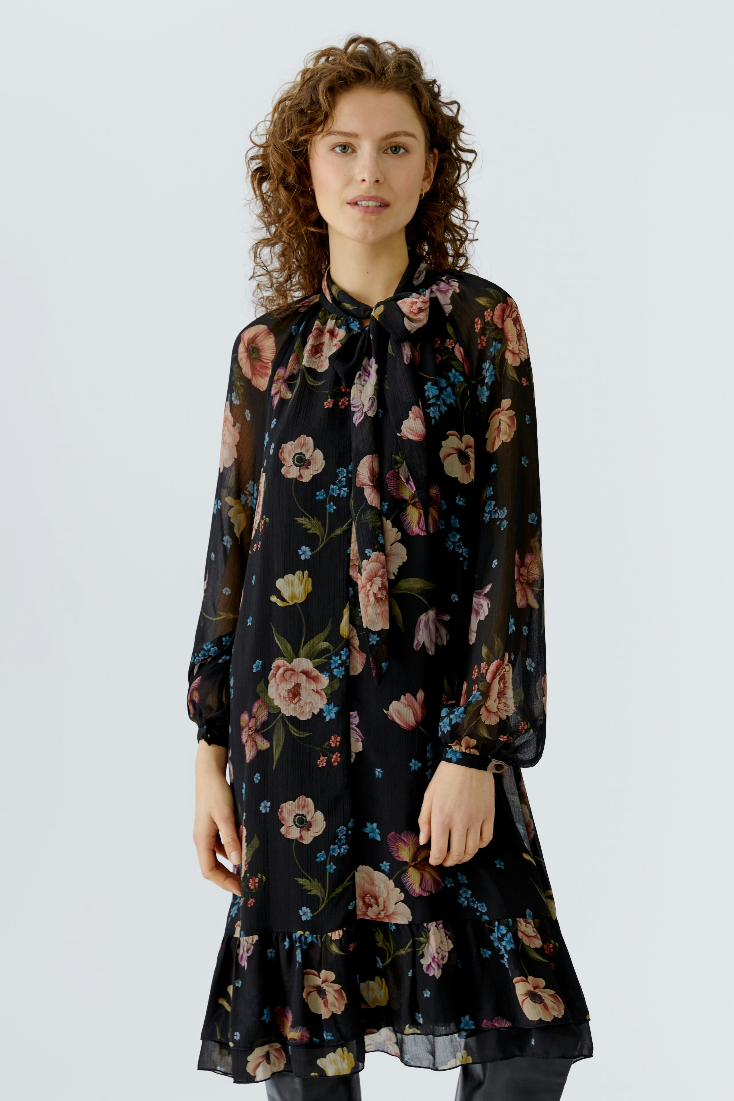 A-line dress: Woman in a black floral dress with long sleeves and a flowing hem, smiling softly.