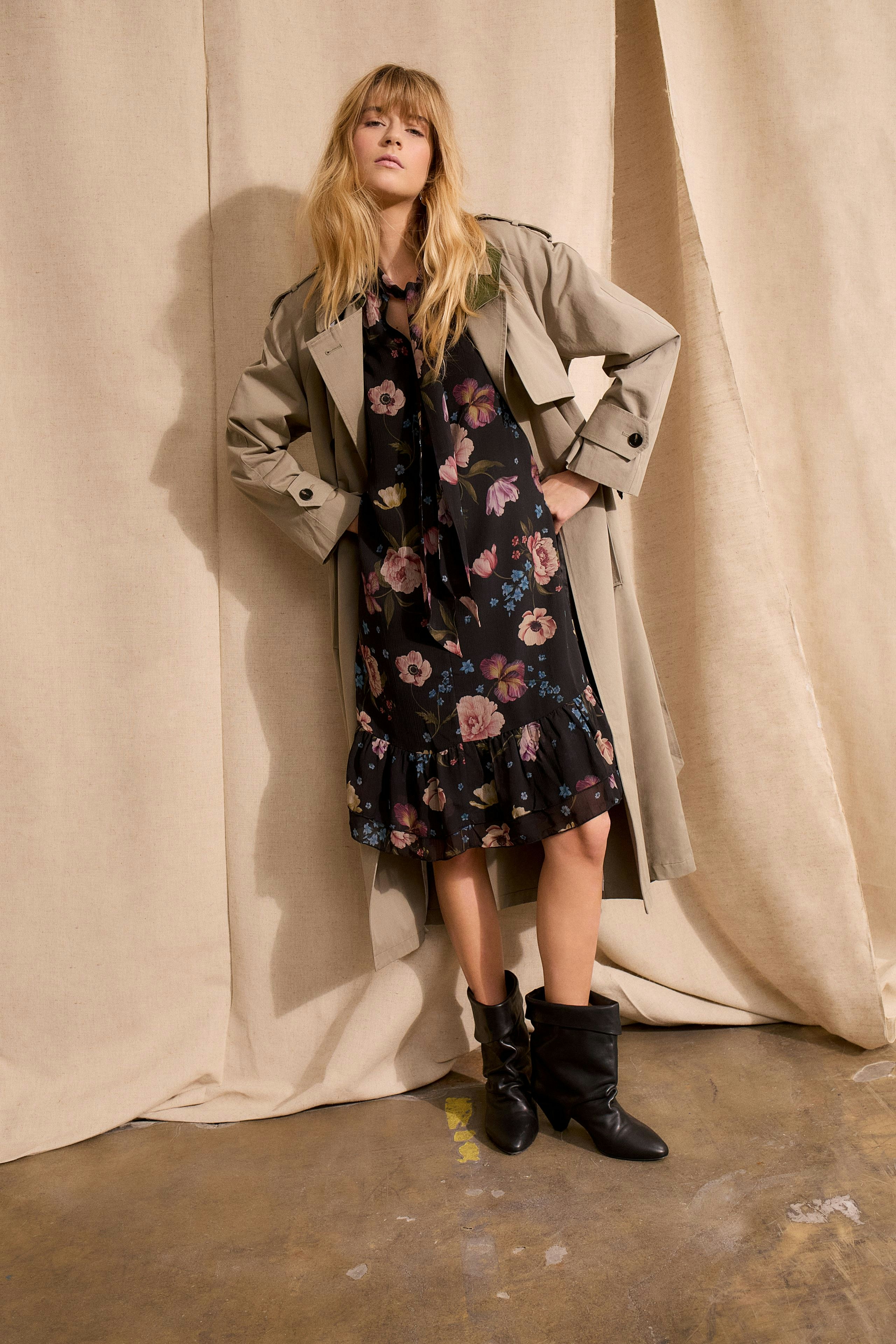 A-line dress: Woman in a floral dress with ruffles, layered under a trench coat and stylish boots.