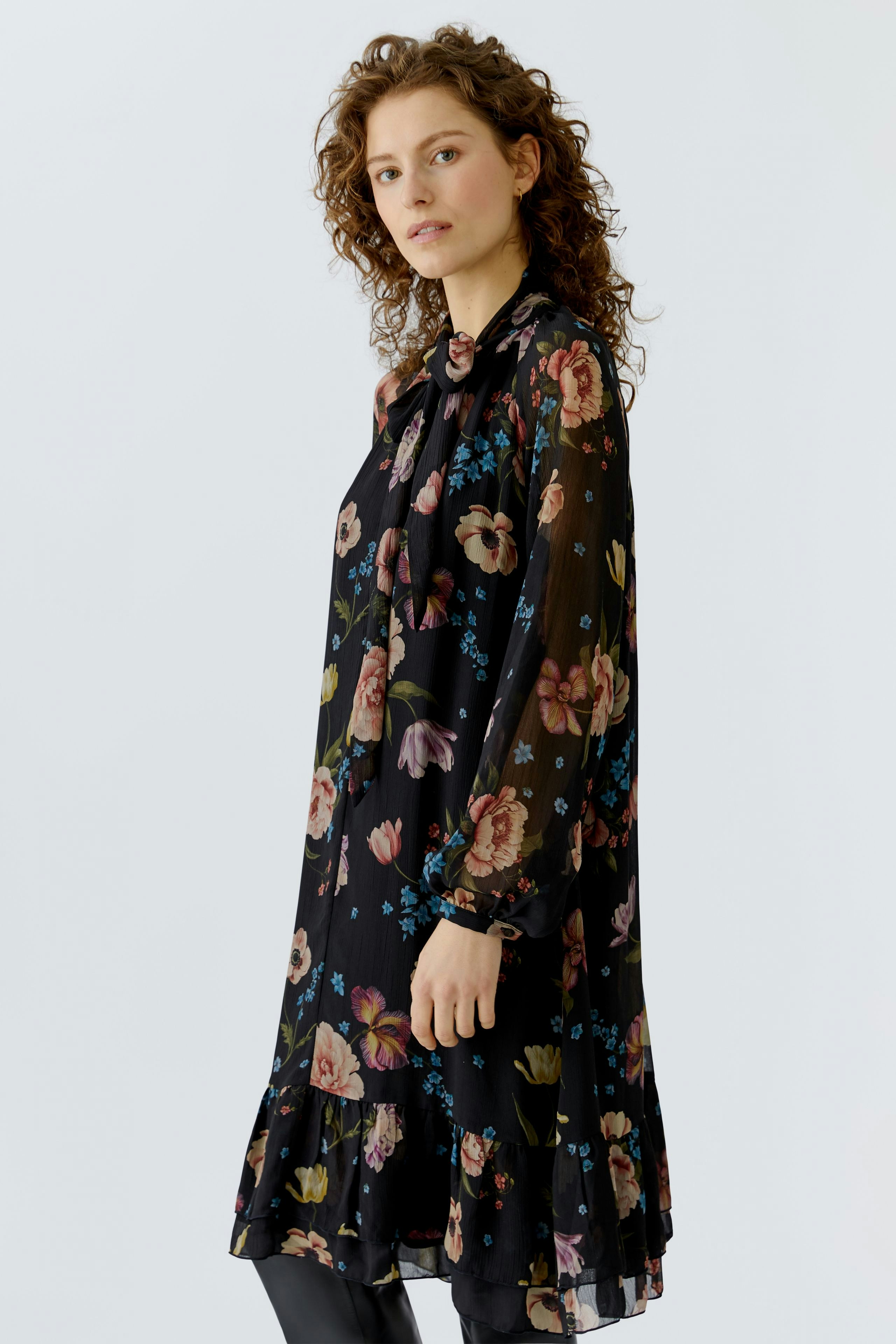 A-line dress: Woman in a black floral dress with long sleeves and a ruffled hem, standing confidently.